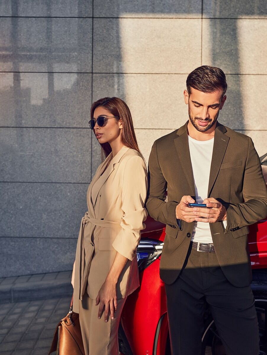 Ein Mann und eine Frau lehnen an einem roten Mercedes-Benz Modell. Der Mann schaut auf ein Telefon.