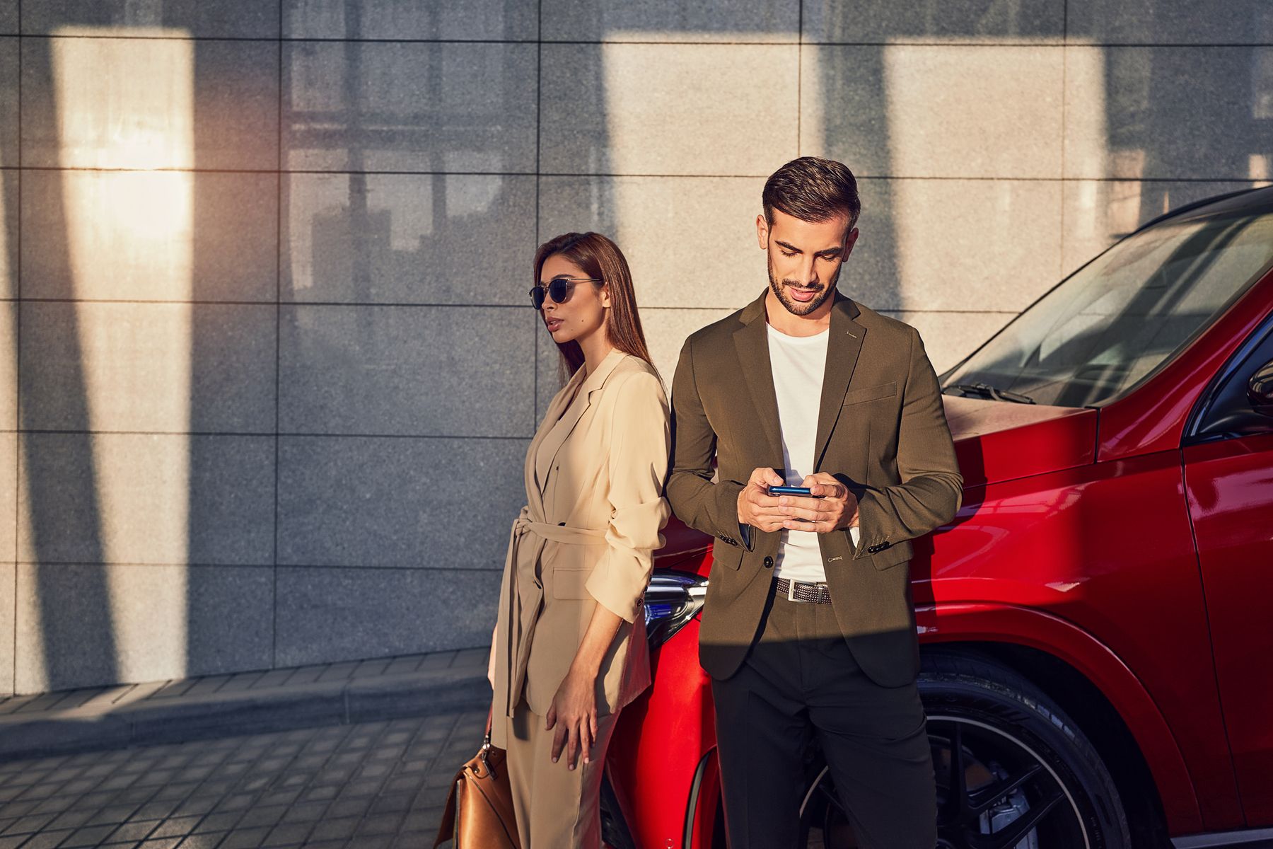Betrug beim Gebrauchtwagenkauf | Mercedes-Benz Ein Mann und eine Frau lehnen an einem roten Mercedes-Benz Modell. Der Mann schaut auf ein Telefon.