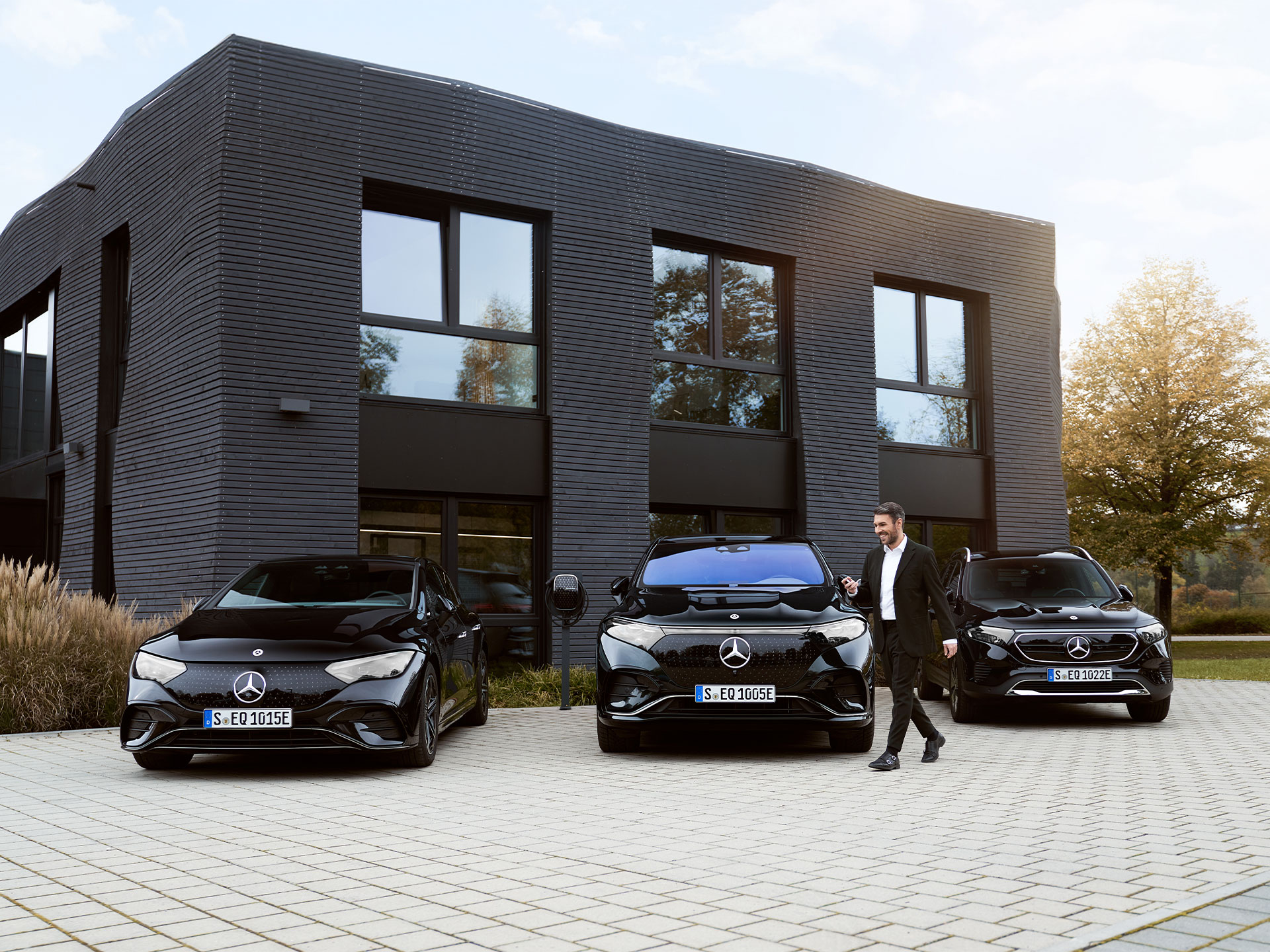 Laden auf dem Betriebshof | Laden | Mercedes-Benz Drei Mercedes-Benz Elektroautos vor einem Bürogebäude.