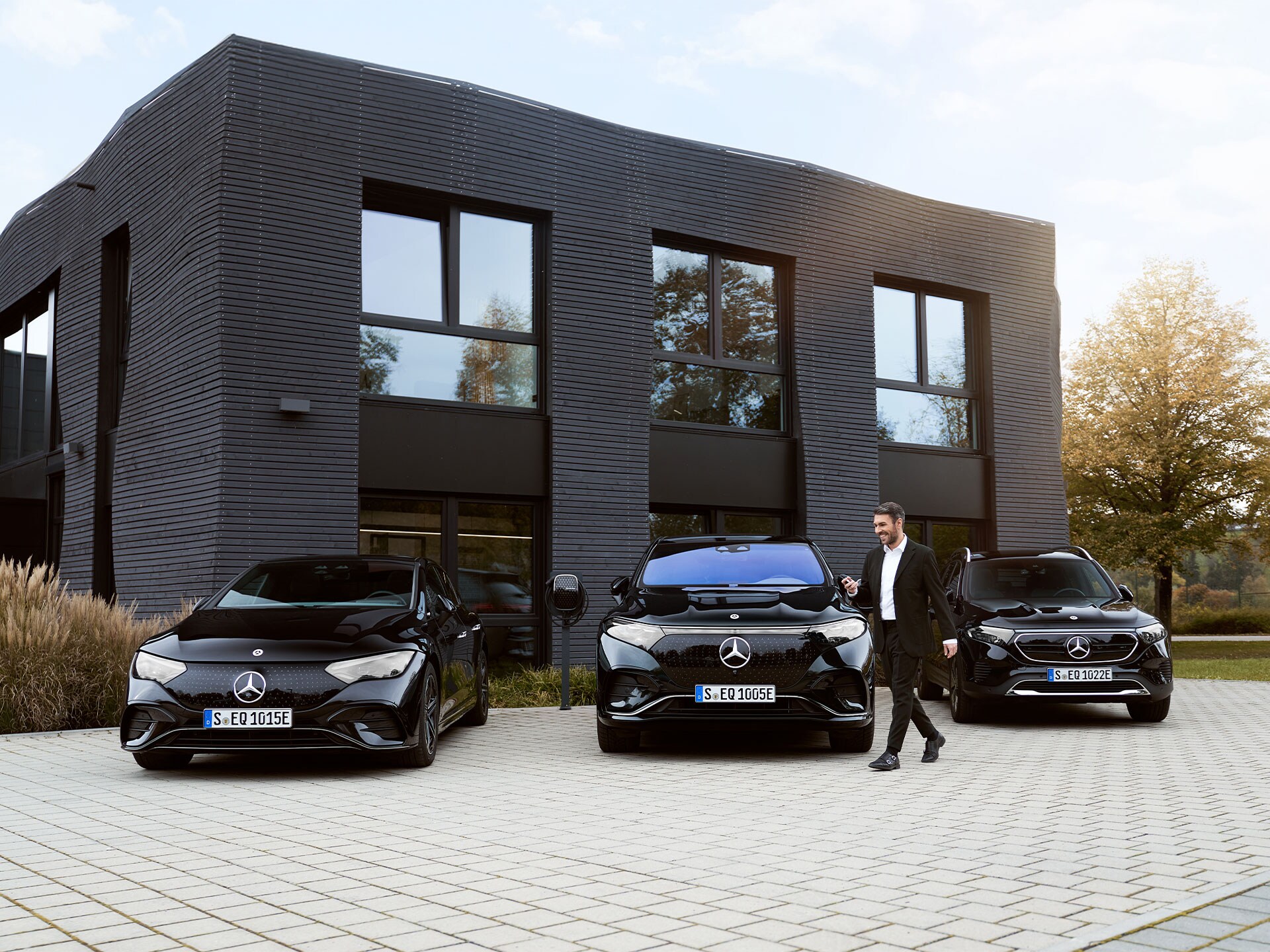 Ein Mann geht an drei geparkten Mercedes-Benz Elektroautos vorbei, die vor einem Bürogebäude stehen.