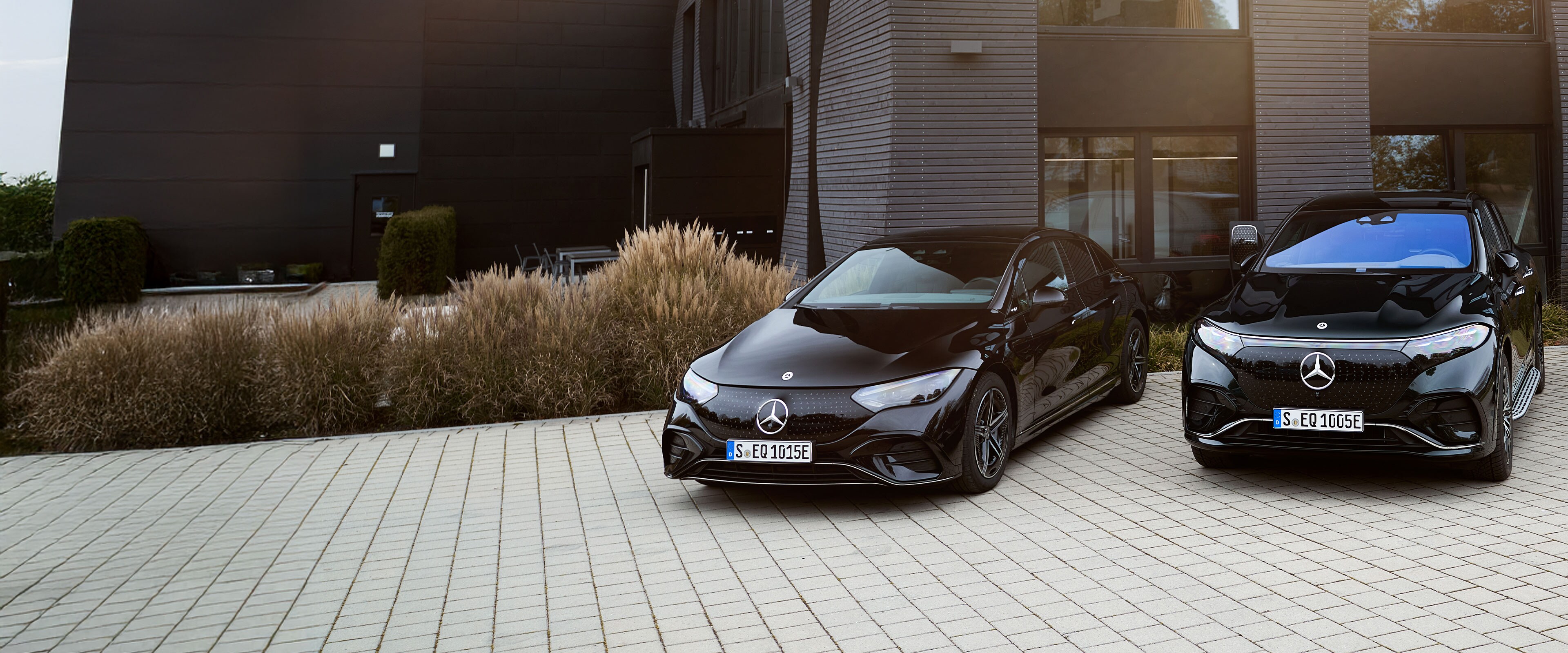 Zwei schwarze Mercedes-Benz Elektrofahrzeuge parken vor einem Betriebsgebäude.