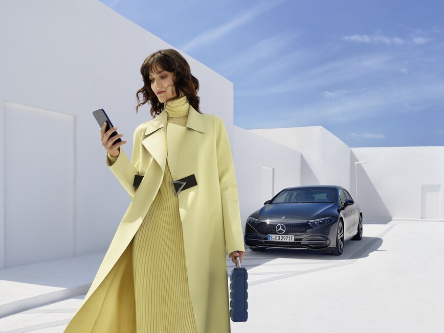 Eine Frau mit ihrem Smartphone steht vor einem Mercedes-Benz.