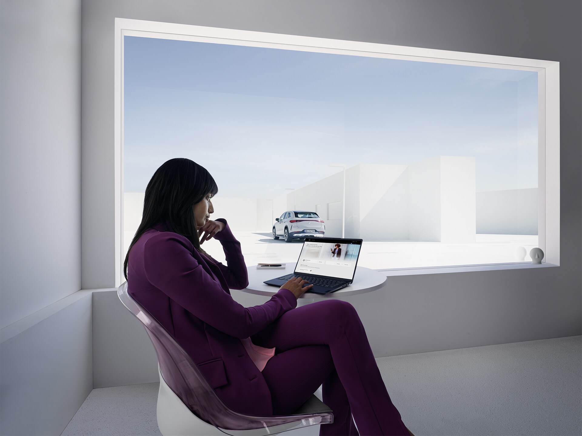 Eine Frau, die an einem Laptop arbeitet, sitzt in einem weißen Büro vor einem großen Fenster.