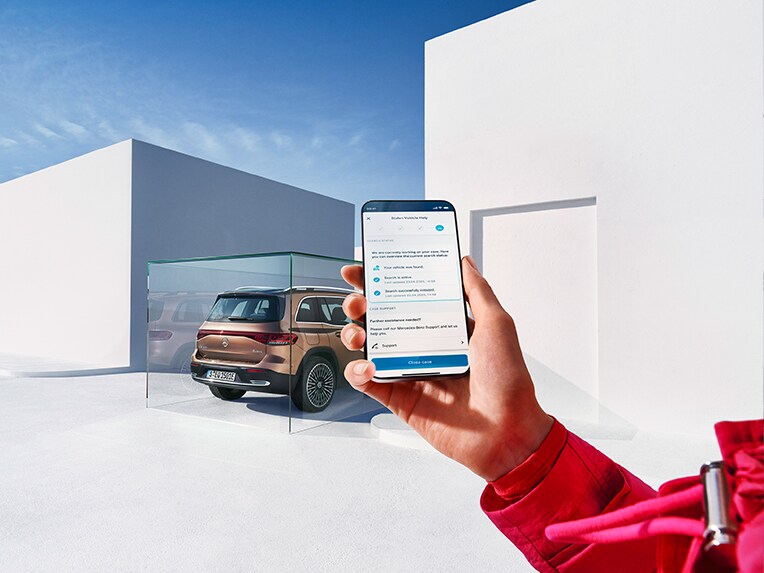 Jemand hält ein Handy in der Hand und benutzt die Mercedes App. Im Hintergrund parkt ein EQB.