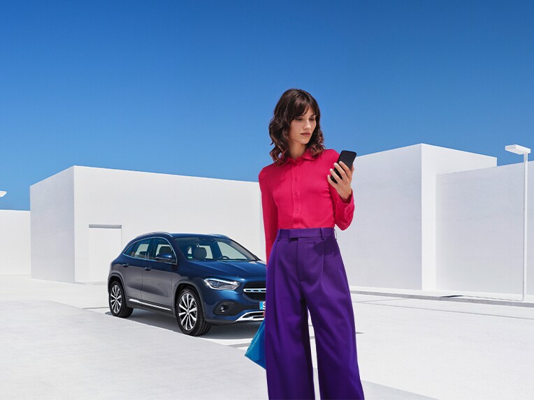 Eine Frau verbindet sich per Smartphone und der Mercedes-Benz App mit ihrem Mercedes Benz und prüft mit den digitalen Extras zum Thema Remote, ob alle Türen ihres Mercedes-Benz verriegelt sind.
