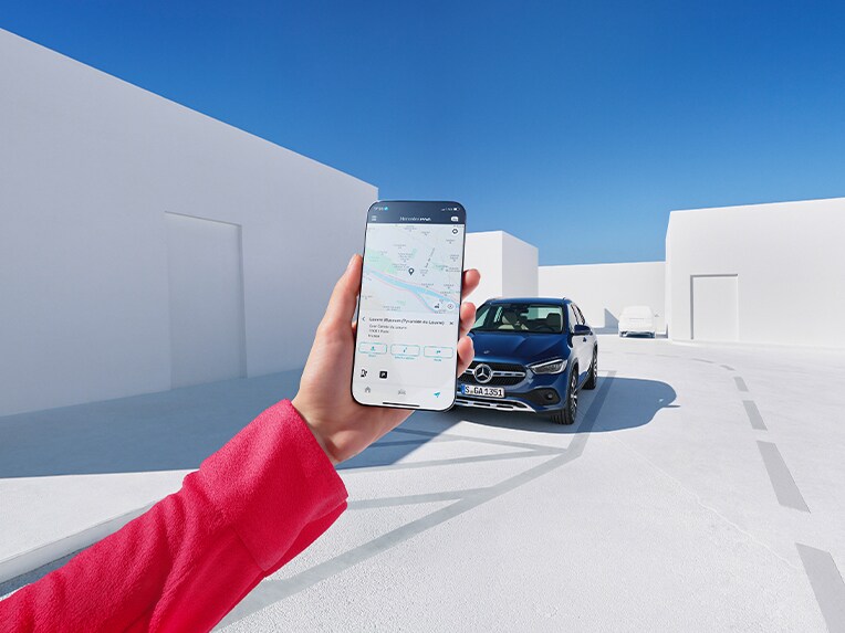 Eine Person hält ein Mobiltelefon in der Hand, auf dem die Mercedes-Benz Service App zu sehen ist. Im Hintergrund steht ein Mercedes-Benz Fahrzeug.