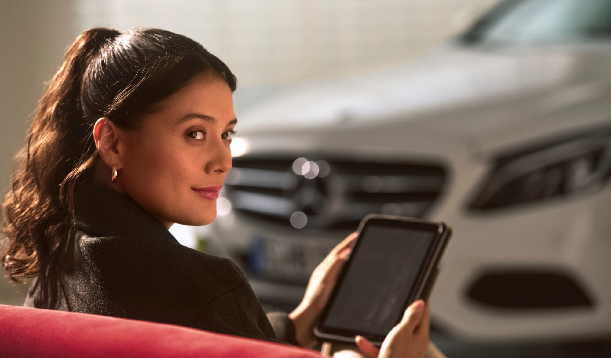 Eine Person sitzt mit einem Tablet in der Hand neben einem Mercedes-Benz Fahrzeug.