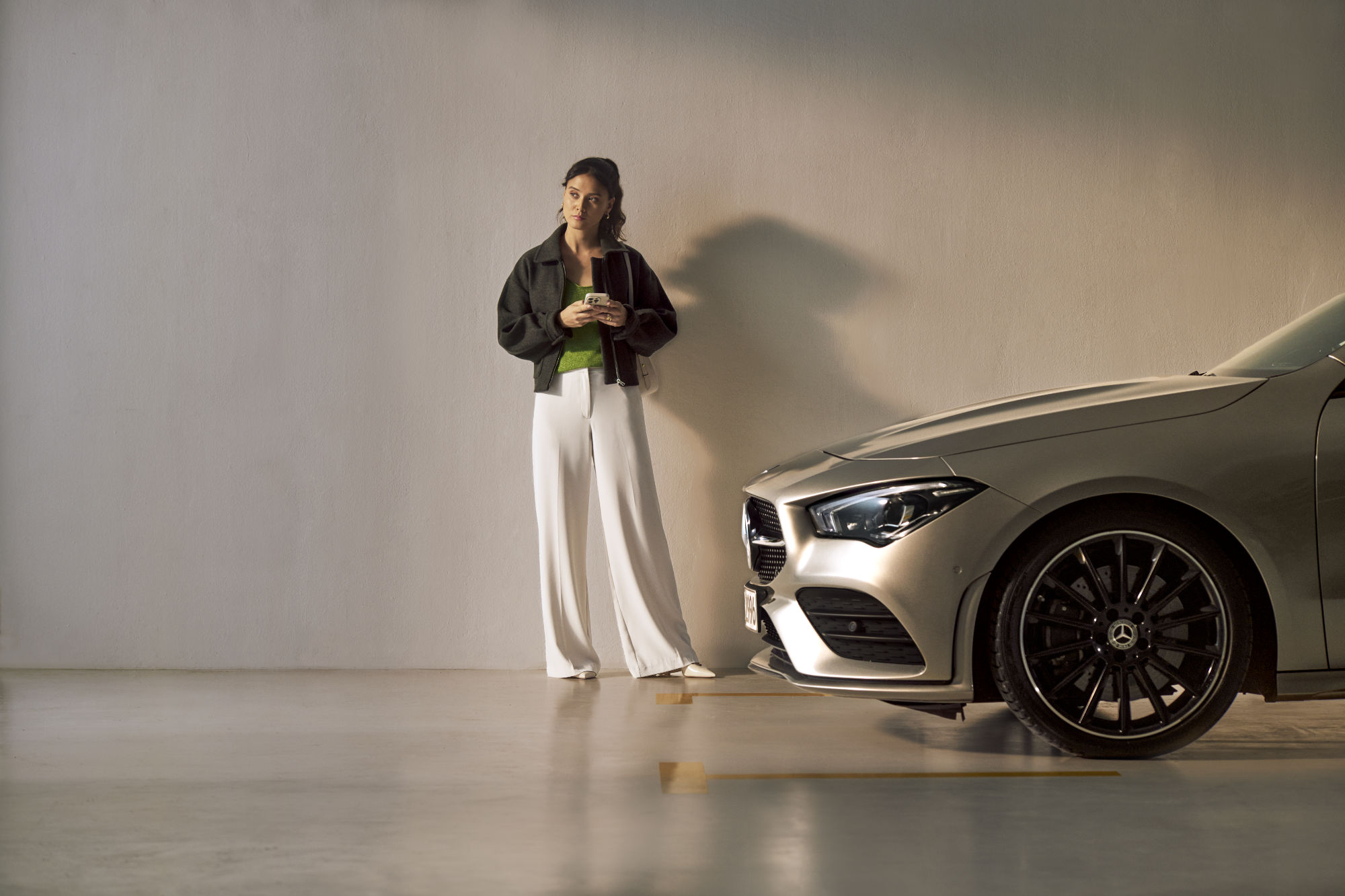 Service VorteilsProgramm | Service Select | Mercedes-Benz. Eine junge Frau steht vor einem Mercedes-Benz Fahrzeug mit Ihren Handy in der Hand und blickt nachdenklich.