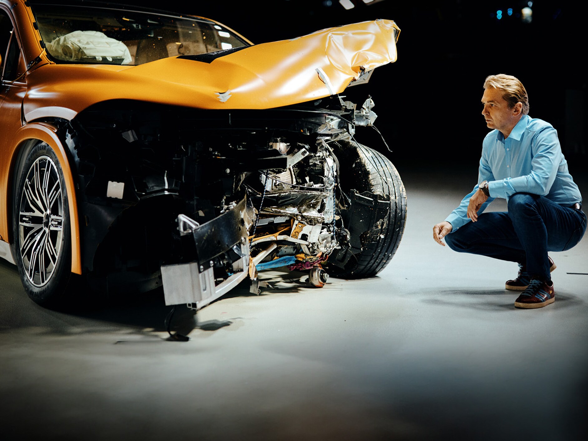 Crashtest-Experte bei der Untersuchung eines frontal beschädigten Mercedes-Benz Fahrzeugs, während er daneben kauert.