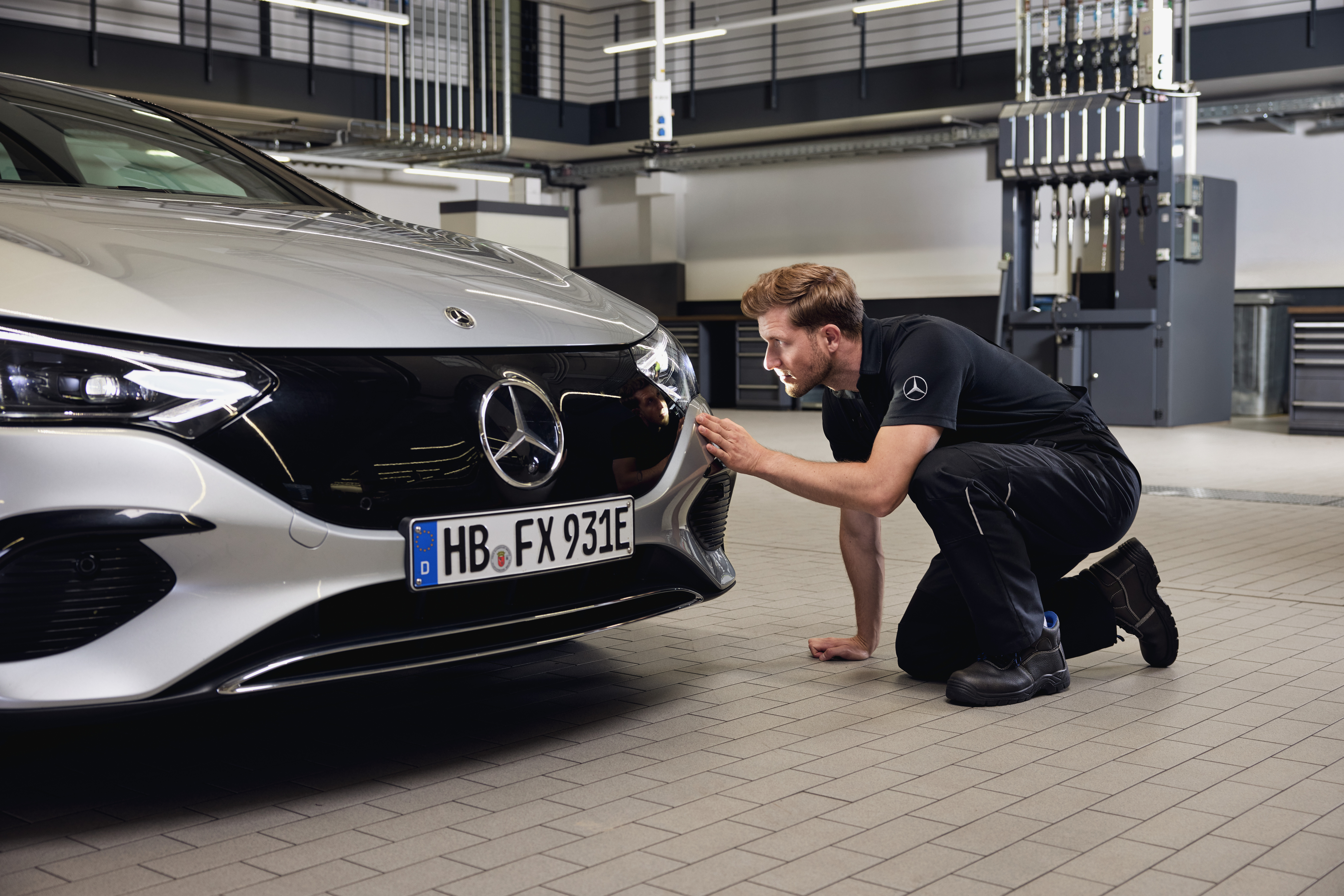 Ersatzteile | Mercedes-Benz Nahaufnahme der Fahrzeugfront eines Mercedes-Benz, an der ein Techniker eine gründliche Prüfung im Zusammenhang mit dem Einbau von Mercedes-Benz Originalteilen durchführt.