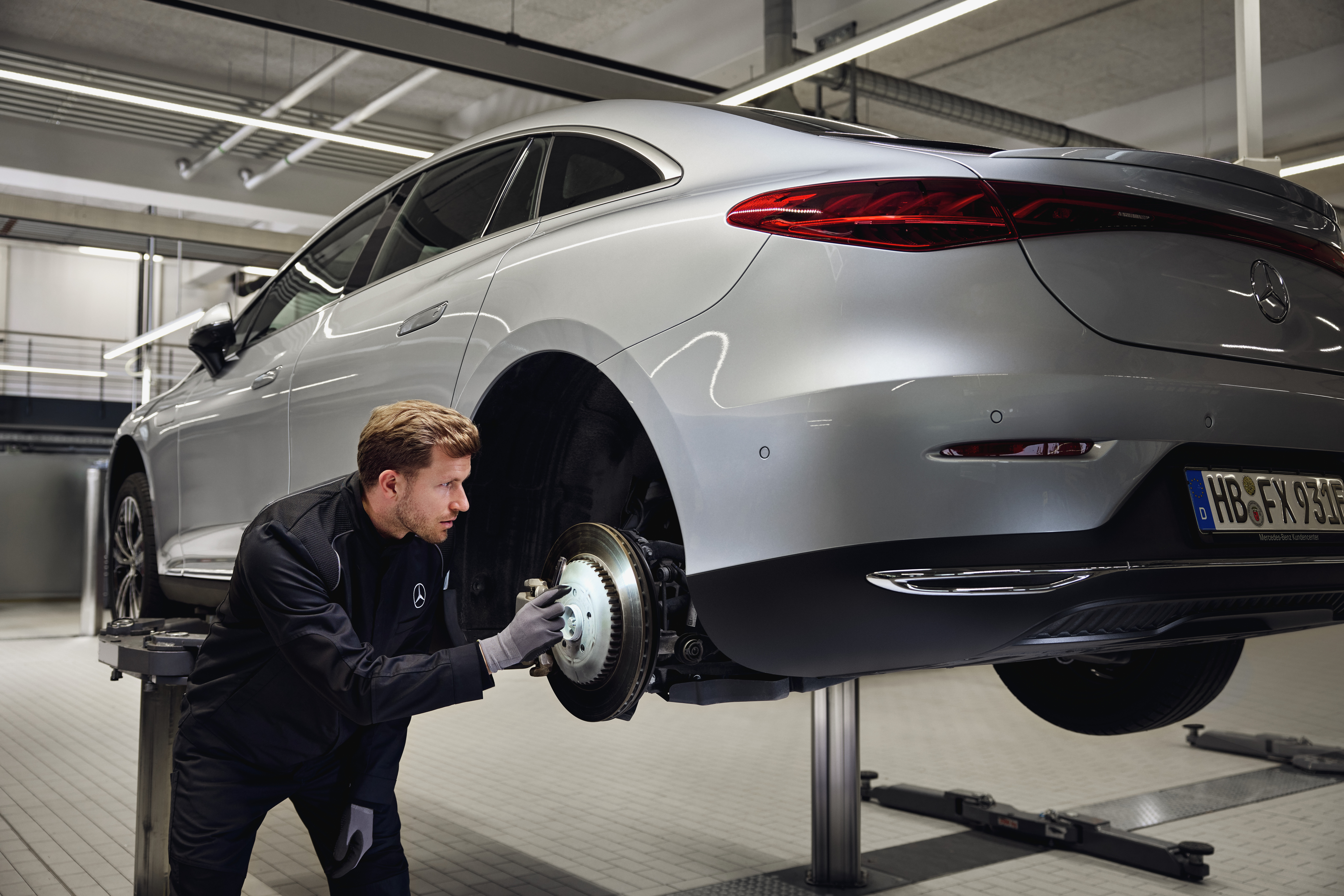 Ersatzteile | Mercedes-Benz Ein Mercedes-Benz-Fahrzeug steht auf einer Hebebühne, während ein Techniker die hintere Bremsanlage im Rahmen eines Austauschs von Originalteilen überprüft.