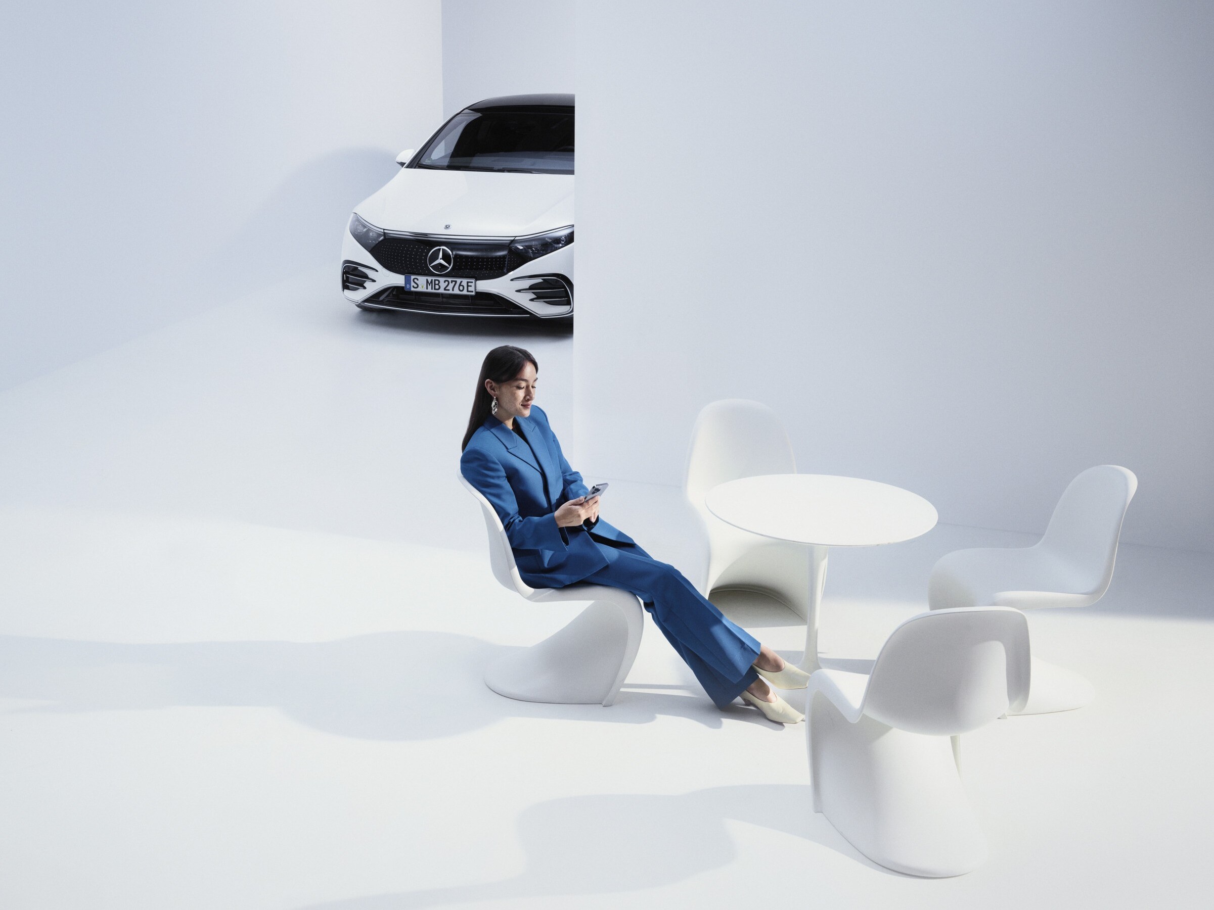 Eine Frau sitzt an einem Tisch und schauf auf ihr Tablet. Im Hintergrund ein Mercedes-Benz SUV.