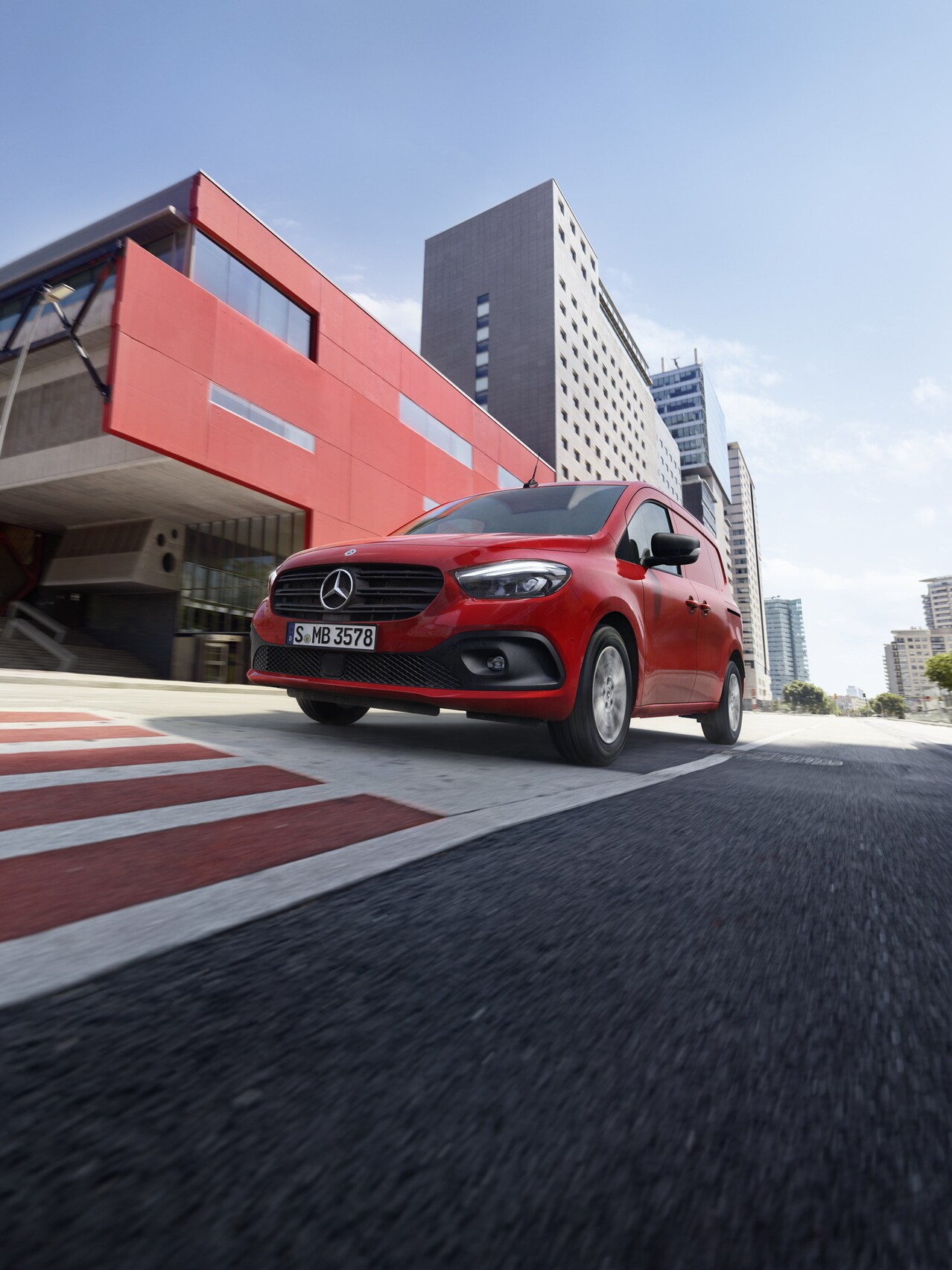 Ein roter Mercedes-Benz Citan Kastenwagen ist auf der Straße unterwegs neben einem roten Gebäude.