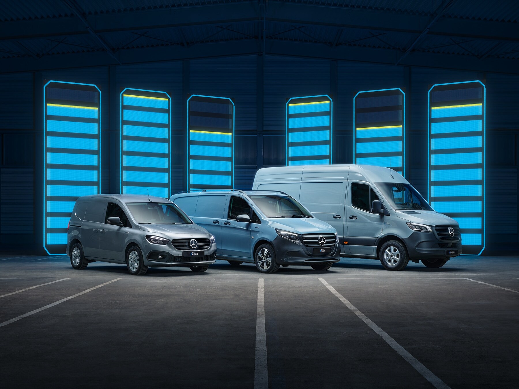 Die Elektrotransporter-Modellpalette von Mercedes-Benz, ausgestellt in einer Lagerhalle mit beleuchteten Ladestationen.