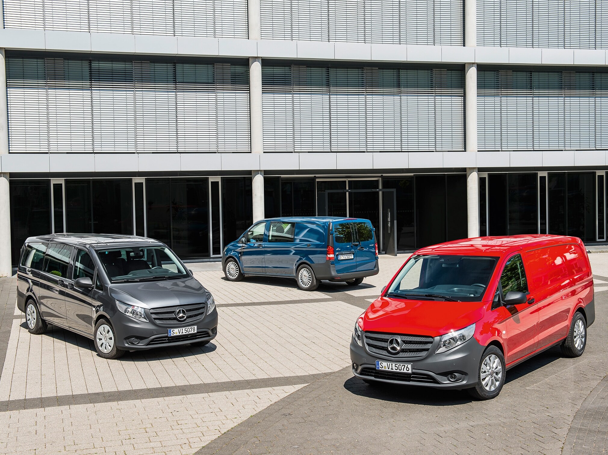 Vor einem modernen Bürogebäude stehen mehrere Mercedes-Benz Vito auf einem sonnigen Parkplatz.