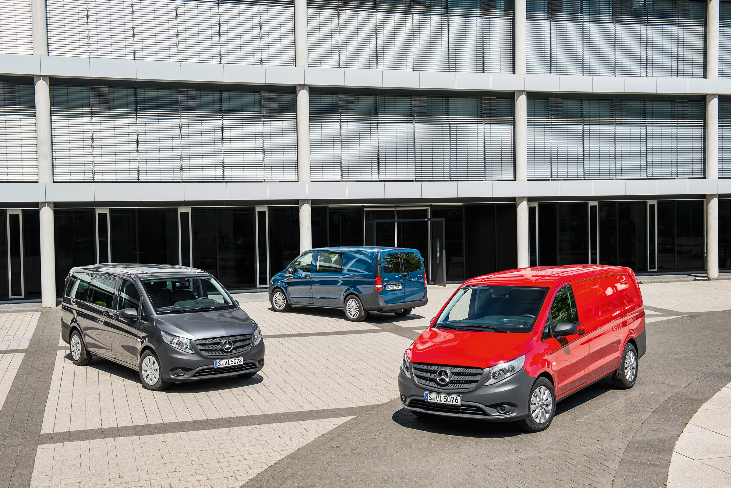 Geschichte | Mercedes-Benz Transporter. Vor einem modernen Bürogebäude stehen mehrere Mercedes-Benz Vito auf einem sonnigen Parkplatz.