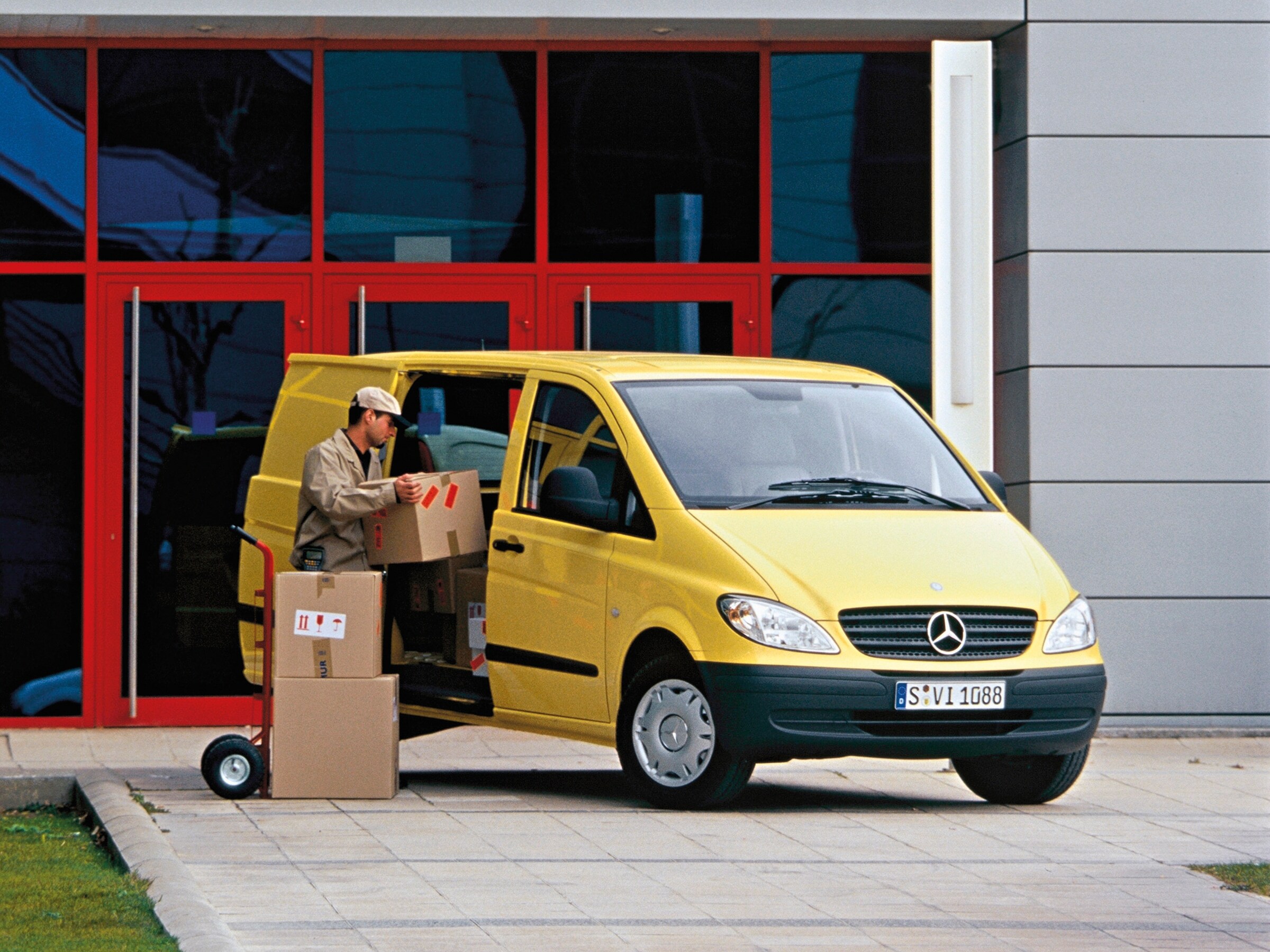 Ein gelber Mercedes-Benz Vito, der vor dem Gebäude geparkt ist, während ein Arbeiter Pakete auslädt.