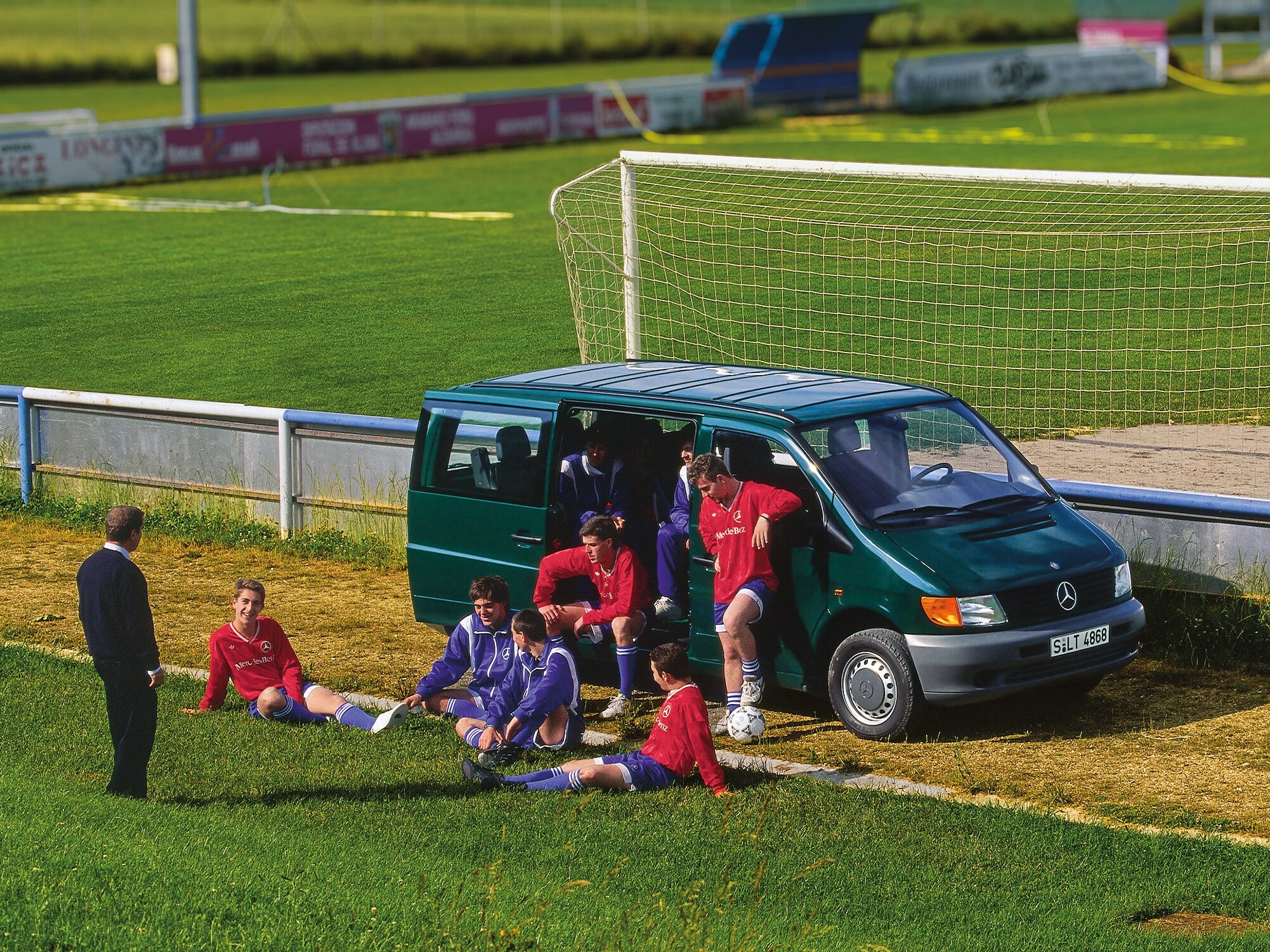 Ein Vito der ersten Generation, der neben einem Fußballplatz geparkt ist, mit Spielern der Mannschaft in der Nähe.