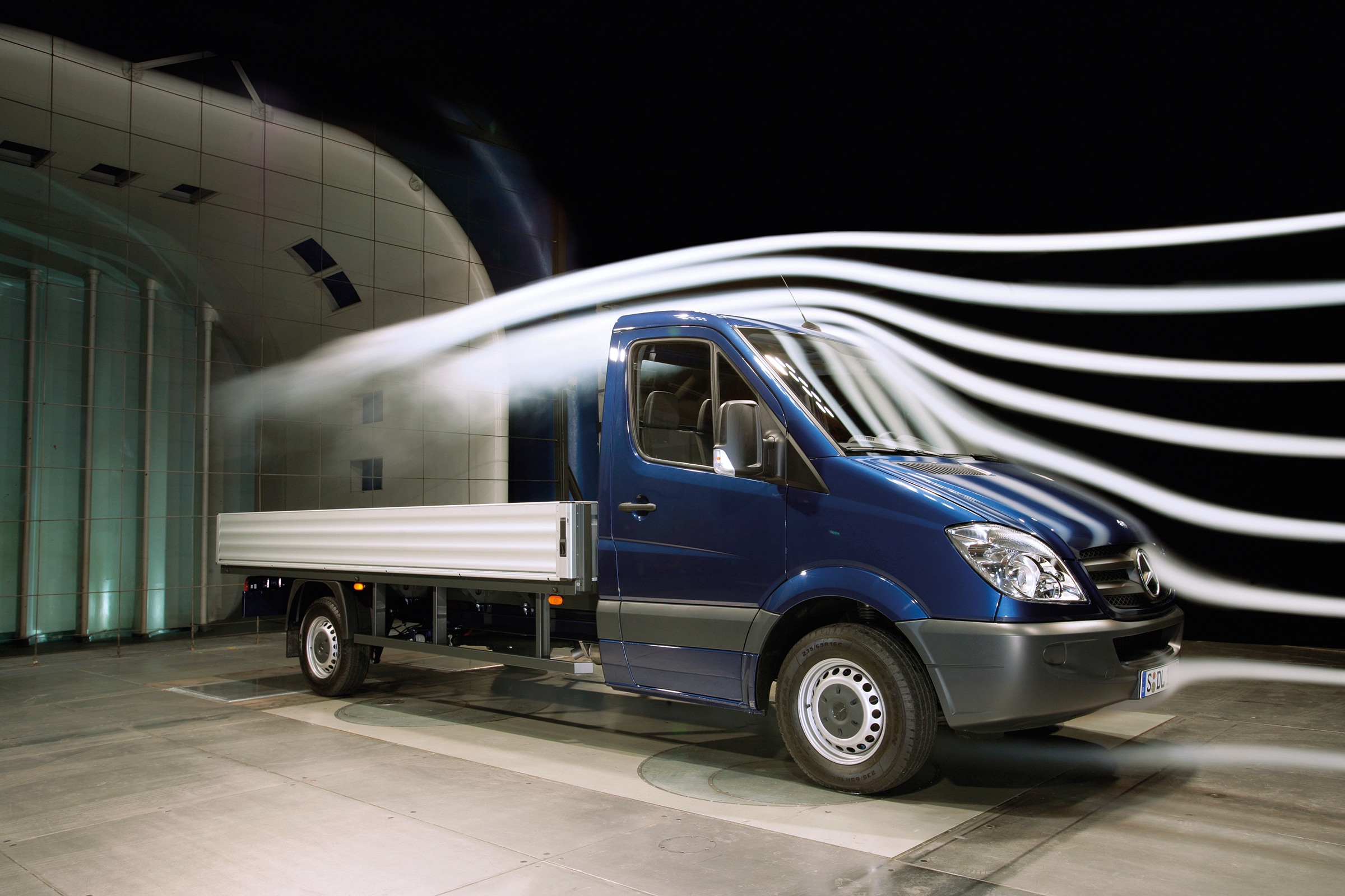 Geschichte | Mercedes-Benz Transporter. Ein blaues Sprinter-Pritschenfahrzeug in einer Windkanal-Testanlage ausgestellt.