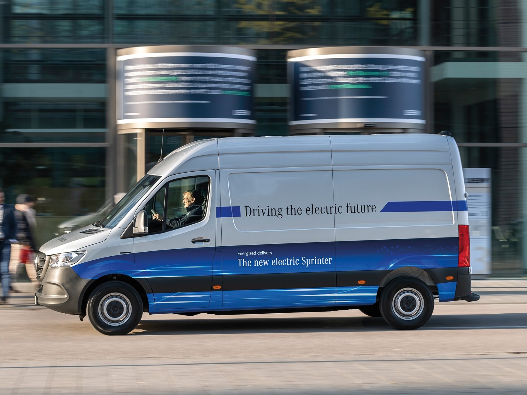 Ein Mercedes-Benz eSprinter Kastenwagen fährt durch eine moderne Stadtstraße.