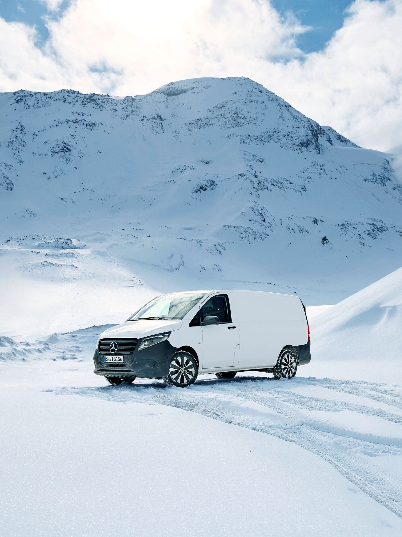 Ein weißer Transporter steht auf dem Schnee zwischen beschneiten Bergen.
