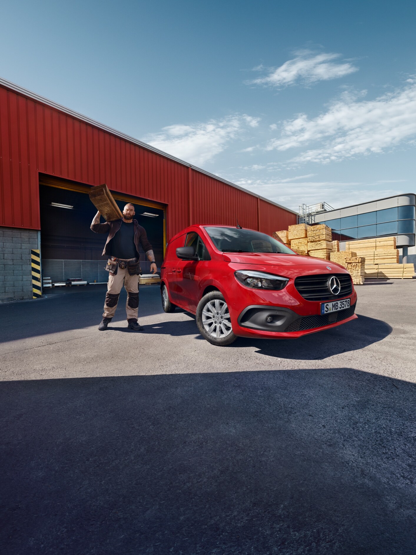 Ein Mercedes-Benz eCitan Kastenwagen steht auf einem Logistikgelände. Daneben eine Person, die Bretter transportiert.