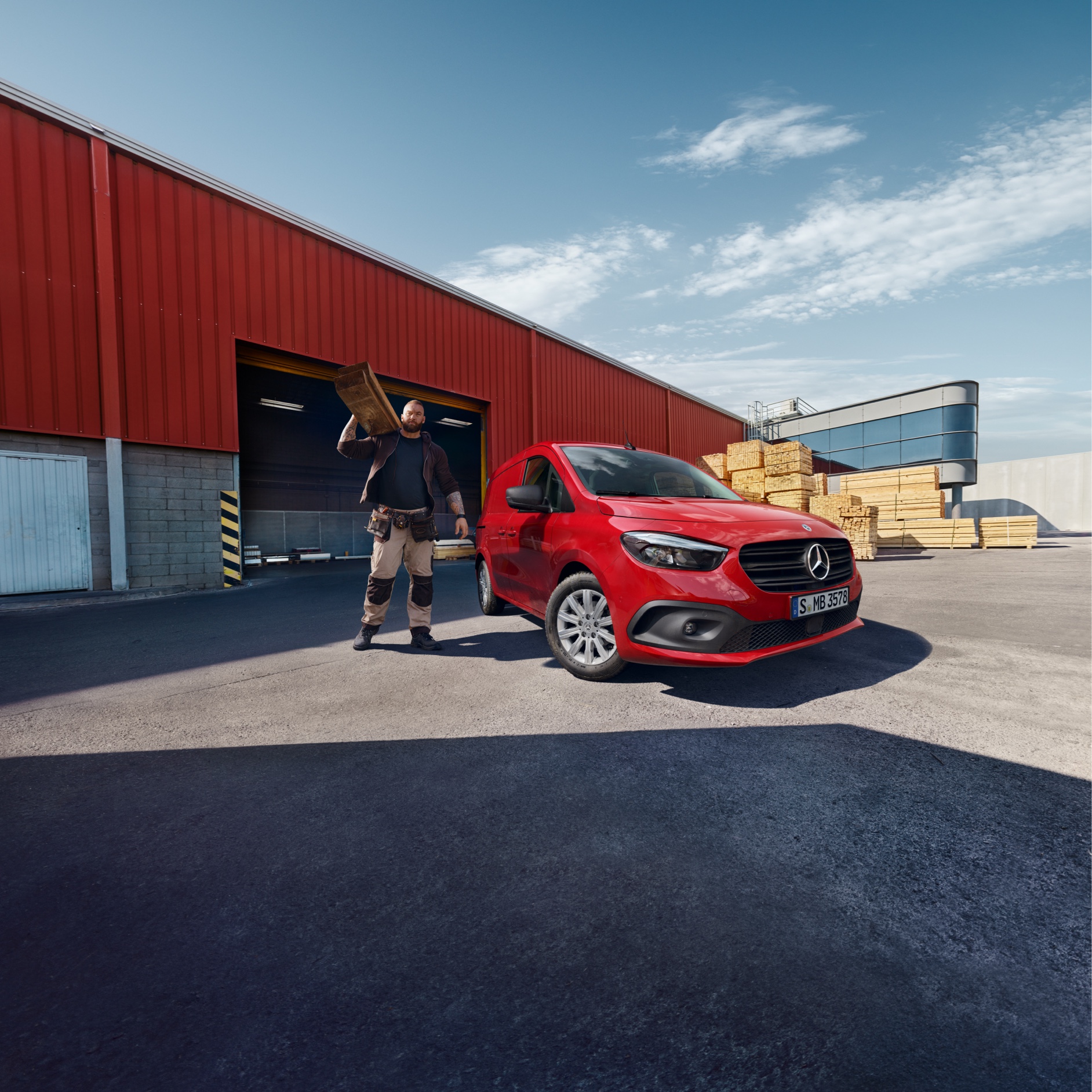 Citan Zuverlässigkeit | Mercedes-Benz Transporter Ein Mercedes-Benz eCitan Kastenwagen steht auf einem Logistikgelände. Daneben eine Person, die Bretter transportiert.