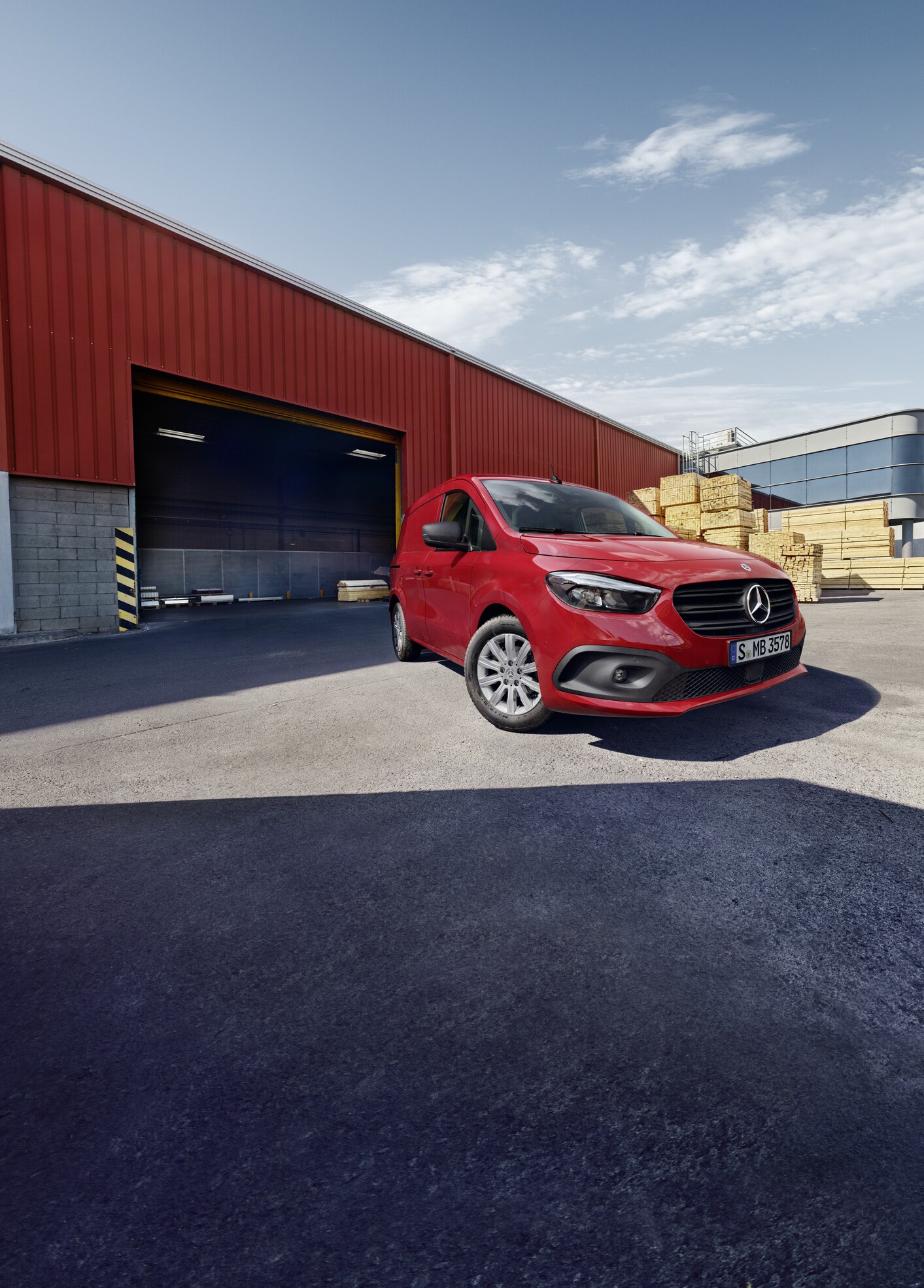 Ein Mercedes-Benz eCitan Kastenwagen steht auf einem Logistikgelände. Daneben eine Person, die Bretter transportiert.