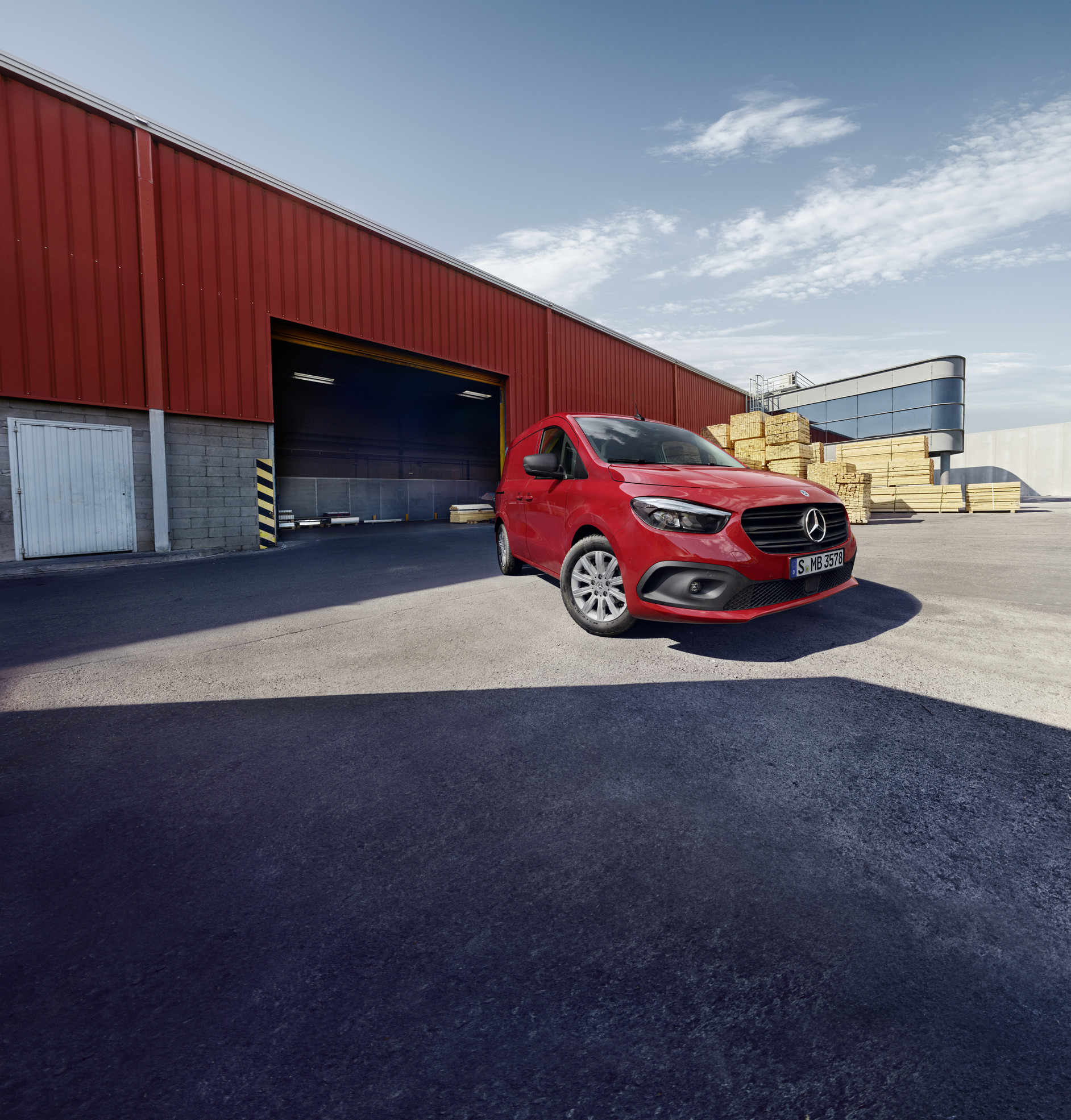 Citan Zuverlässigkeit | Mercedes-Benz Transporter Ein Mercedes-Benz eCitan Kastenwagen steht auf einem Logistikgelände. Daneben eine Person, die Bretter transportiert.