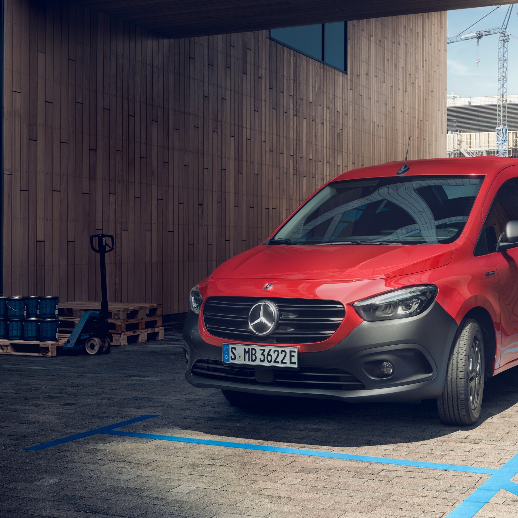 Der eCitan Kastenwagen, ein elektrischer Transporter von Mercedes-Benz, parkt an einer Ladesäule vor einem modernen Gebäude.