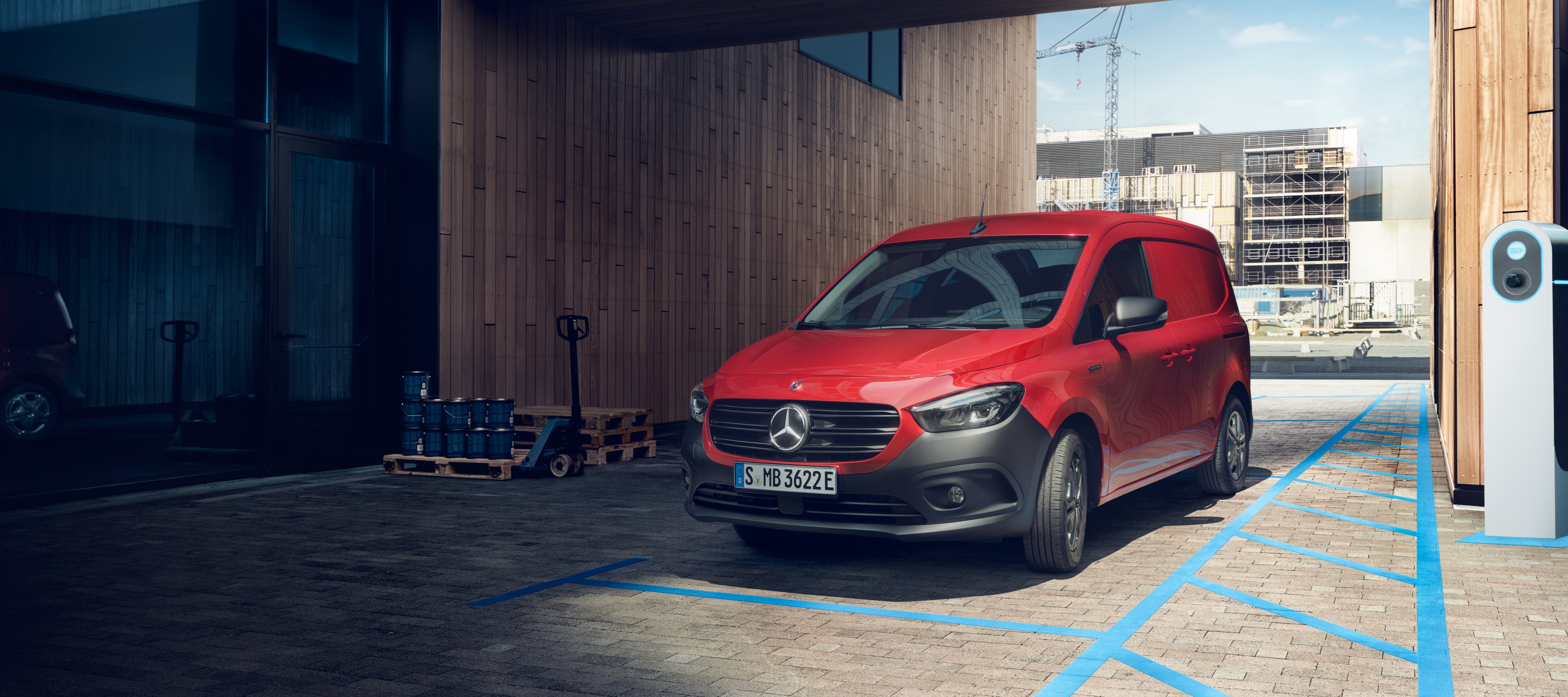eCitan Kastenwagen | Mercedes-Benz Transporter Der eCitan Kastenwagen, ein elektrischer Transporter von Mercedes-Benz, parkt an einer Ladesäule vor einem modernen Gebäude.