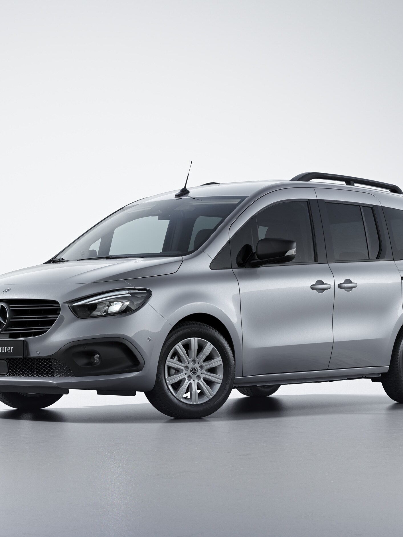 Ein silbergrauer Mercedes-Benz Citan Tourer in der Ausstattungslinie PRO in seitlicher Frontansicht auf hellgrauem Untergrund.