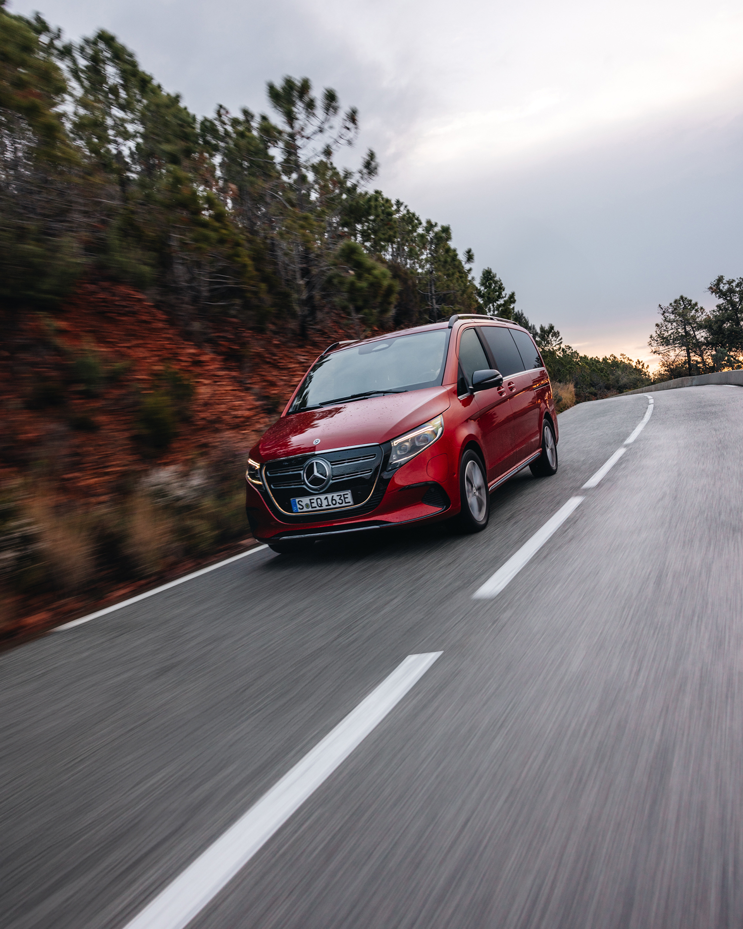 Modellübersicht | EQV | Mercedes-Benz Ein roter Mercedes-Benz EQV fährt eine Landstraße hinab.