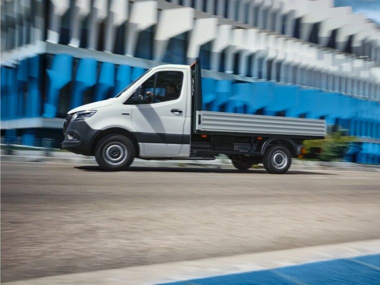 Das Mercedes-Benz eSprinter Fahrgestell als Pritschenfahrzeug fährt vor einem Gebäude entlang.