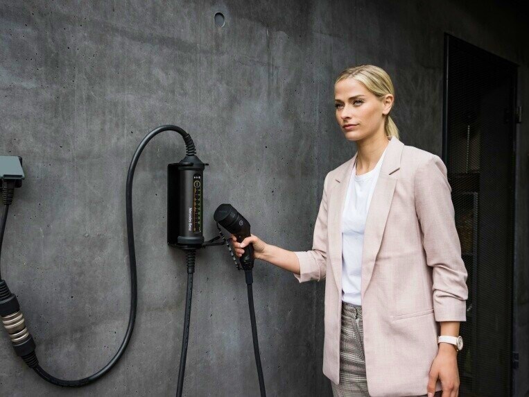 Eine Frau hält den Ladestecker, der mit einer Box an der Wand verbunden ist.
