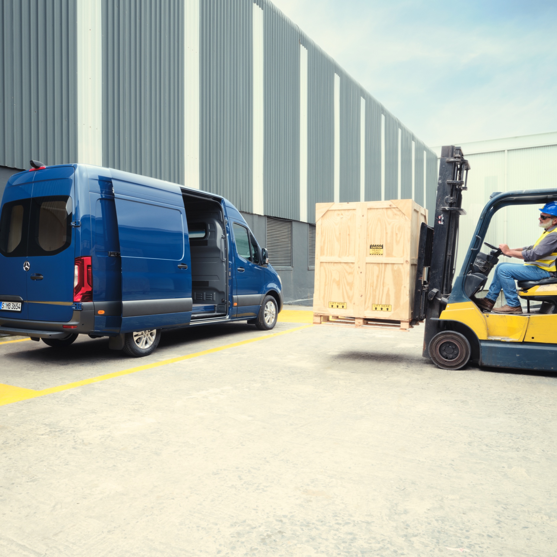 Alle Sprinter-Modelle | Mercedes-Benz Transporter Ein blauer Mercedes-Benz Sprinter Kastenwagen wird von einem Gabelstapler beladen.