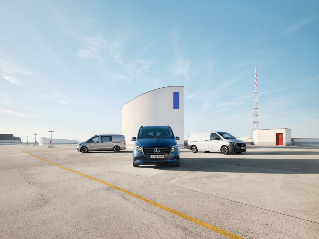 Drei Mercedes-Benz Vitos stehen auf einem großen Parkplatz vor einem modernen weißen Gebäude.