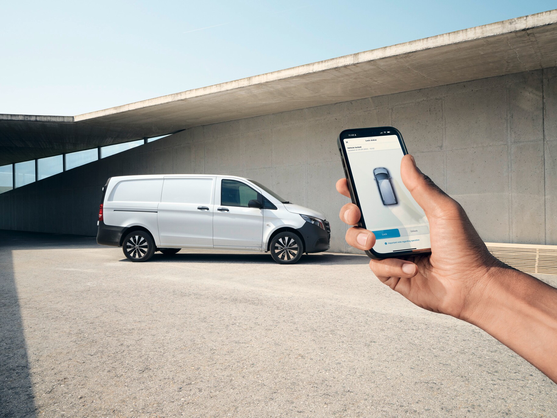 Eine Hand hält ein Smartphone hoch, dass die Mercedes-Benz App zeigt. Vito Kastenwagen im Hintergrund.