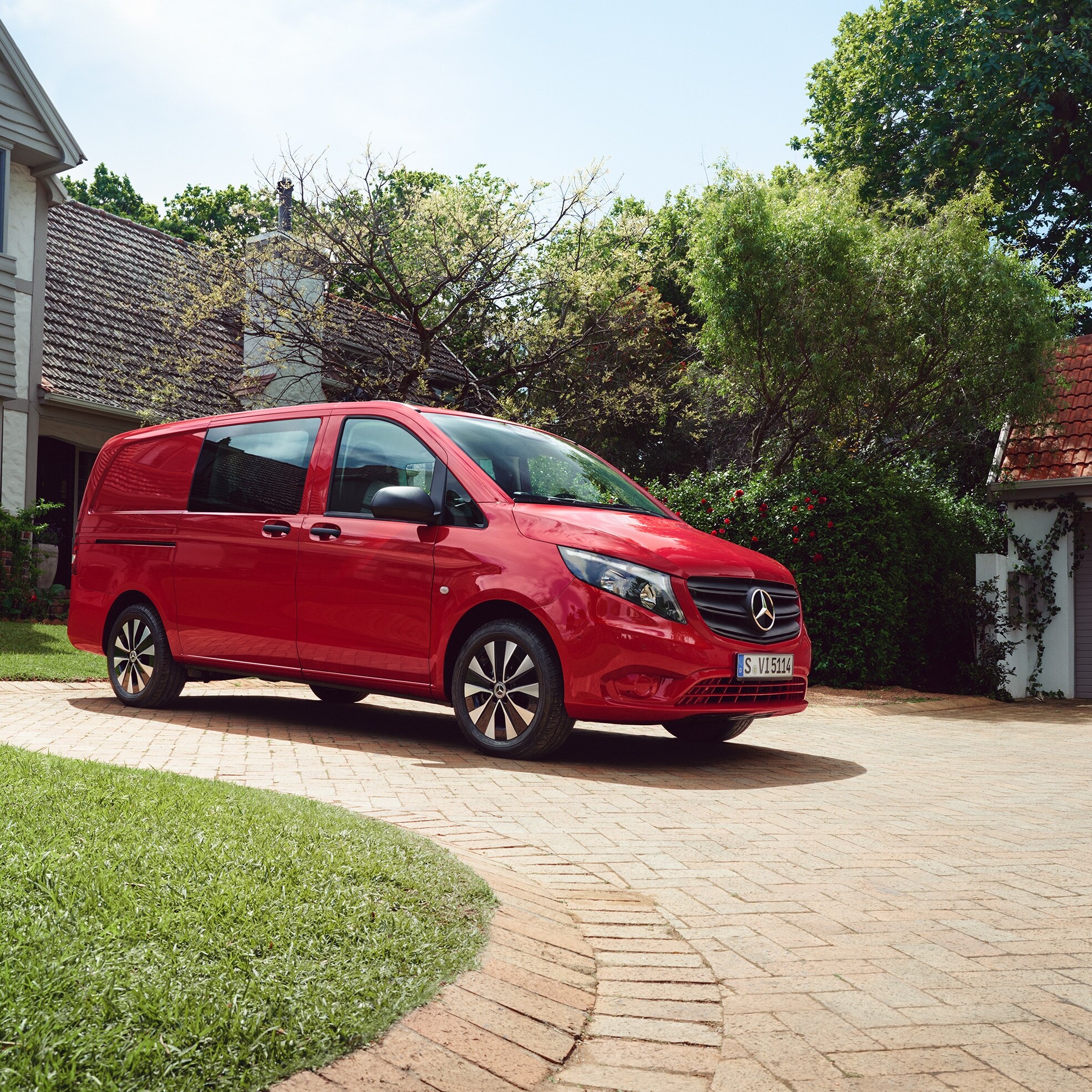 Ein roter  Mercedes‑Benz Vito Mixto parkt auf einer gepflasterten Einfahrt vor einem Haus mit grünem Garten.