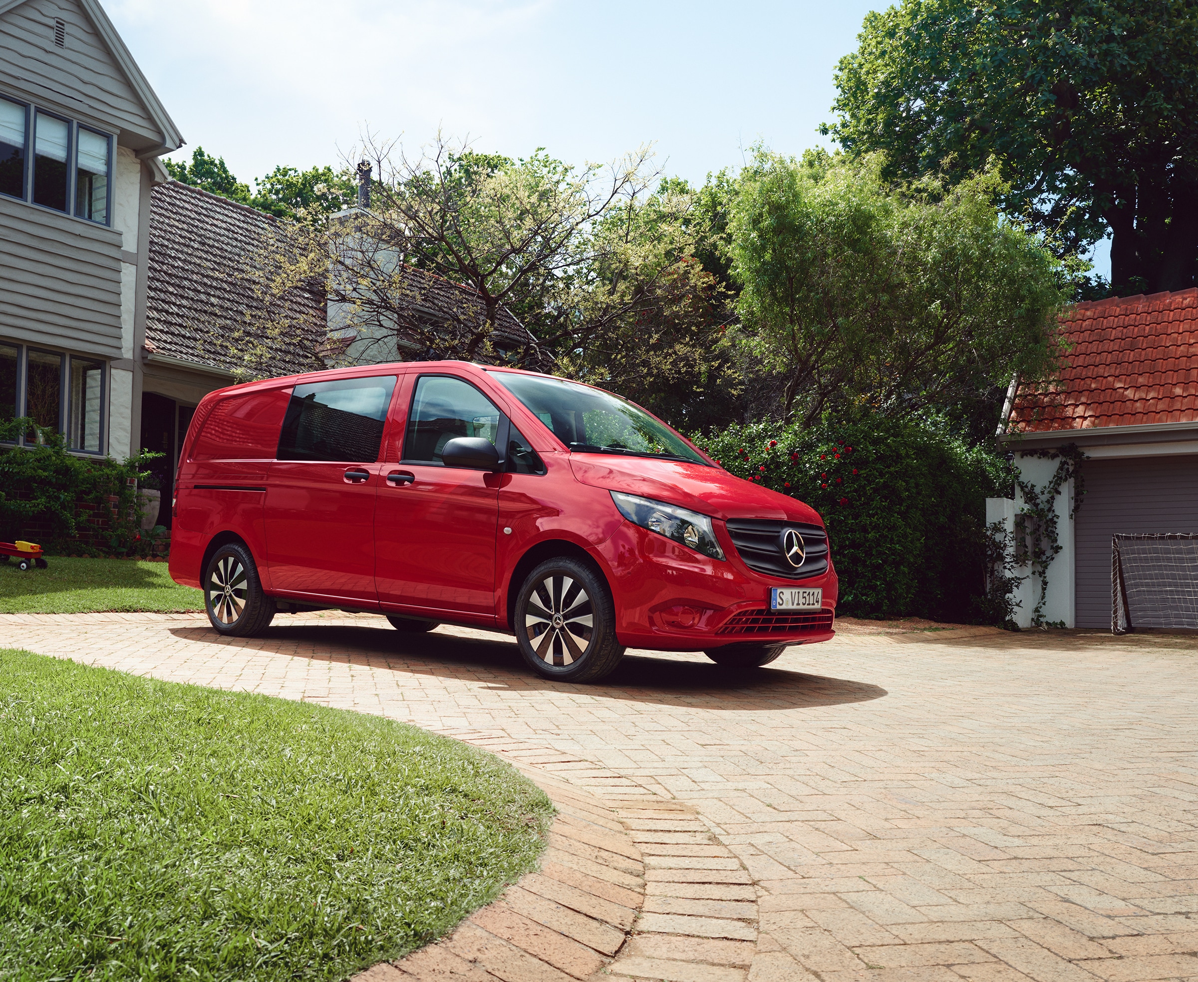 Vito Mixto | Alle Vito-Modelle | Mercedes-Benz Transporter Ein roter Mercedes‑Benz Vito Mixto parkt auf einer gepflasterten Einfahrt vor einem Haus mit grünem Garten.