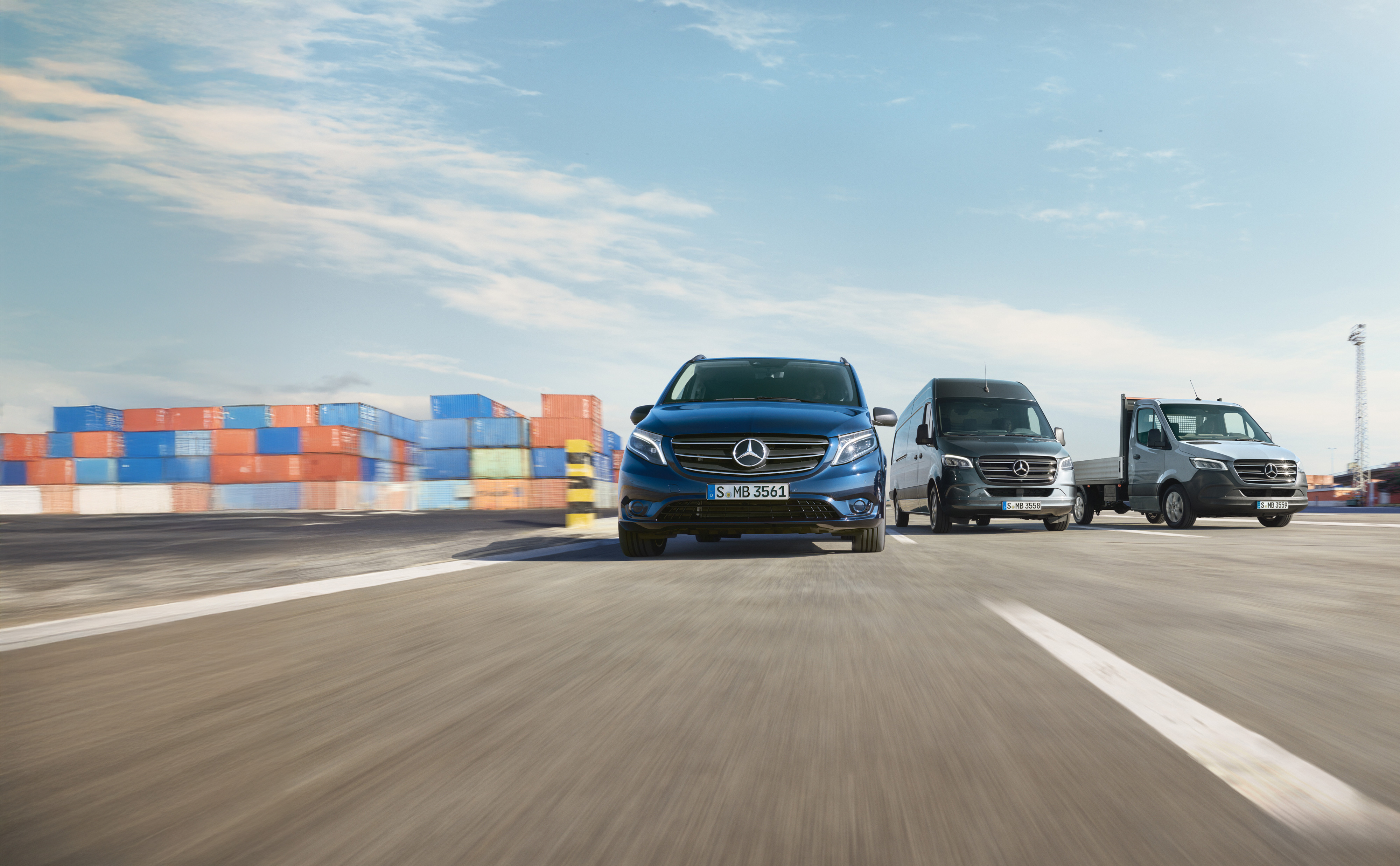 Service24h | Mercedes-Benz Transporter. Eine Reihe von Mercedes-Benz Transportern, die nebeneinander auf einer Straße neben einer Laderampe geparkt sind.