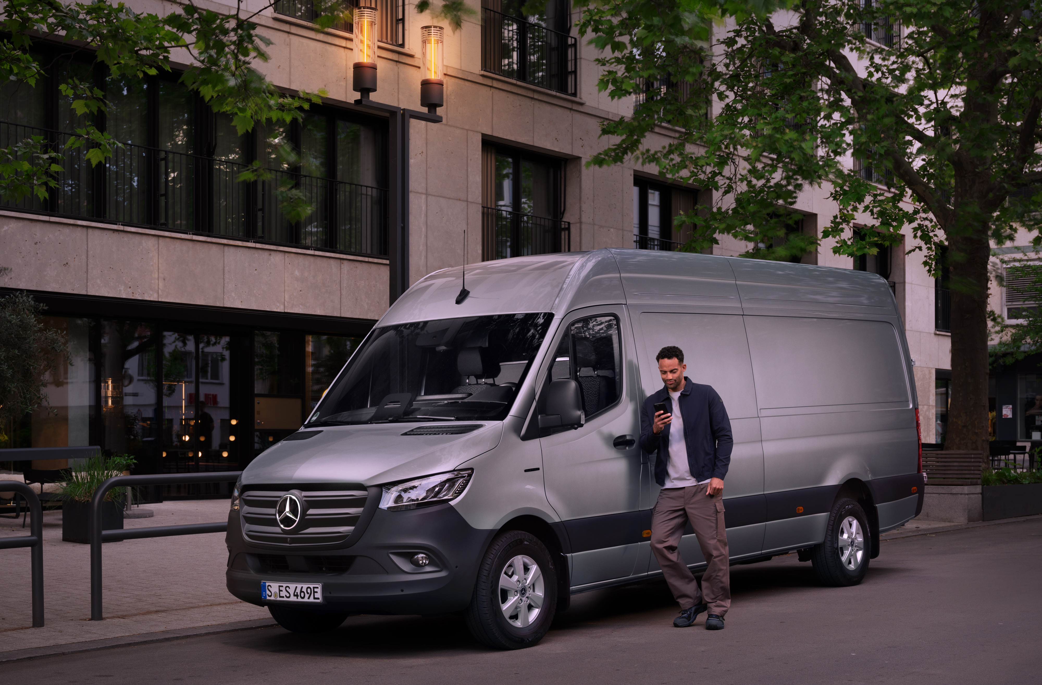 Customer Assistance Center | Mercedes-Benz Transporter. Mann lehnt am Mercedes-Benz Van und nutzt sein Smartphone – schnelle Hilfe durch Mercedes-Benz Kundenbetreuung.