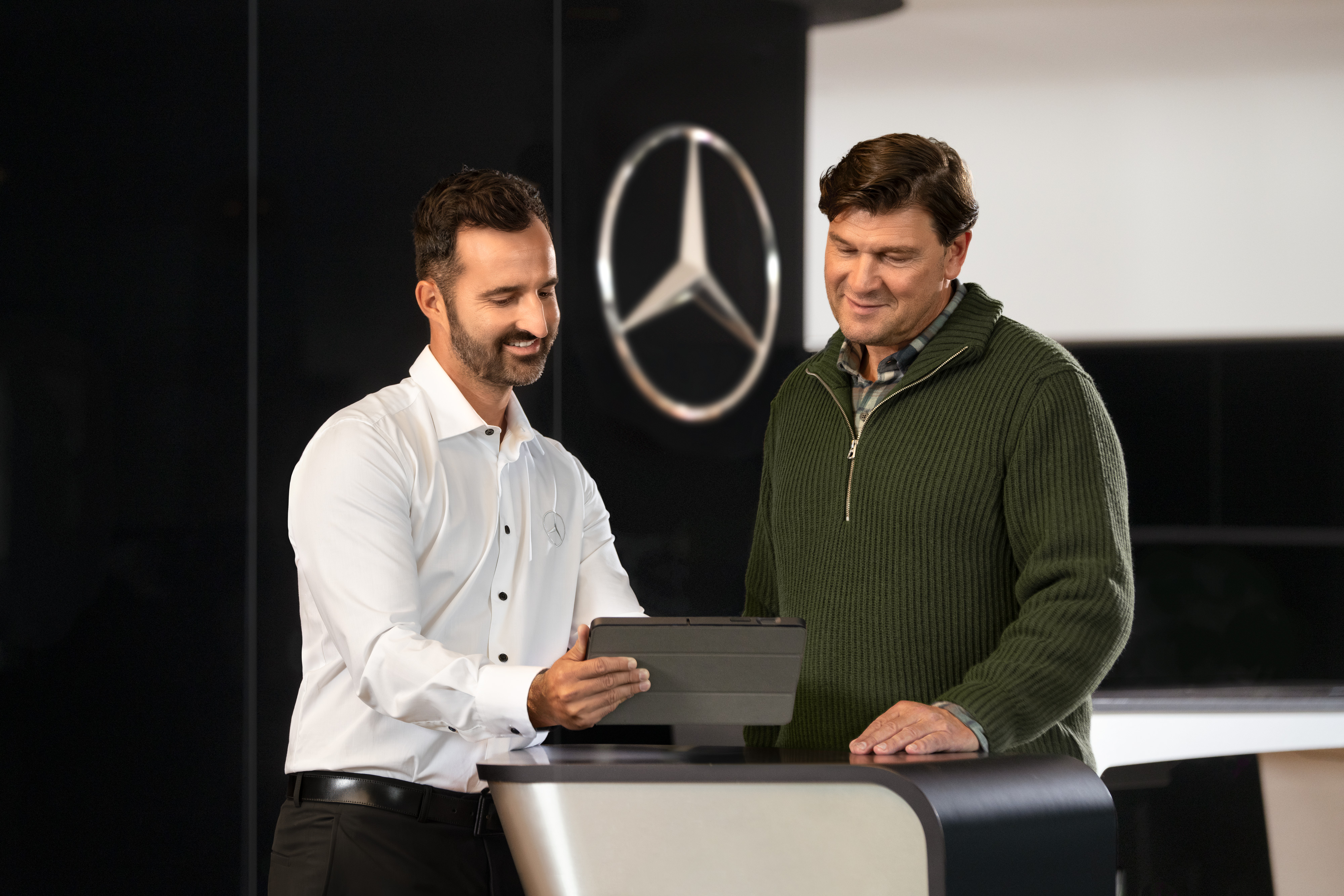 Individuelle Betreuung | Mercedes-Benz Transporter. Mercedes-Benz Mitarbeiter berät Kunden am Tresen mit Tablet – individuelle Betreuung und Gewerbeberatung im Autohaus.
