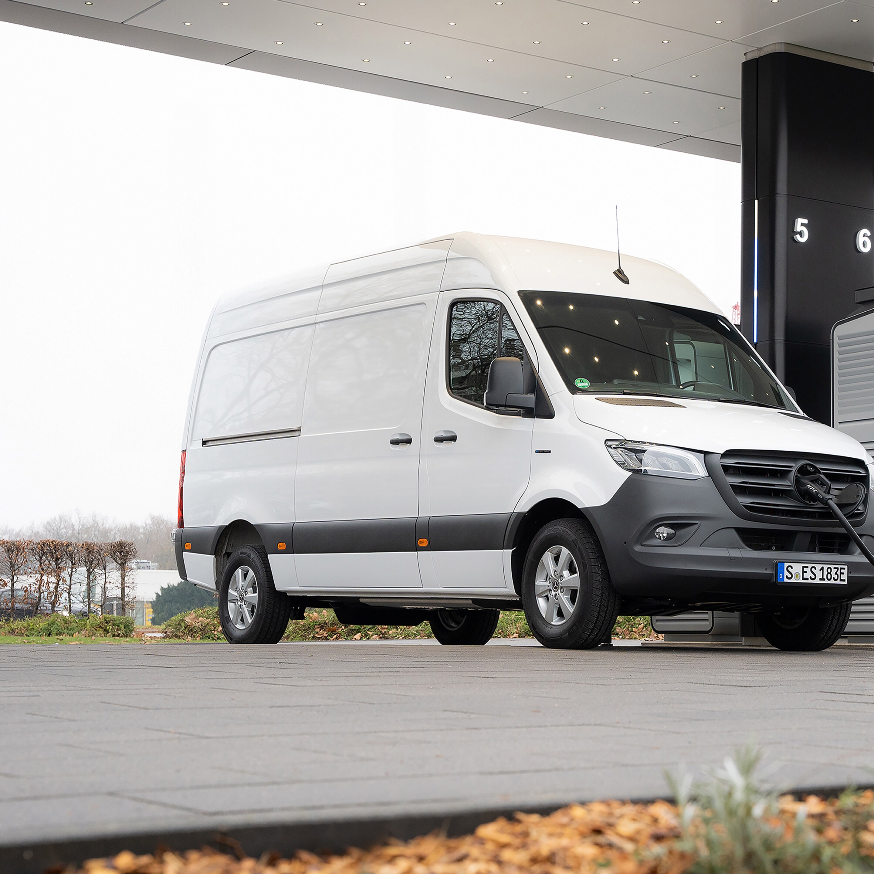 Eine weißer eSprinter Kastenwagen steht an einer Ladesäule be trübem Wetter.