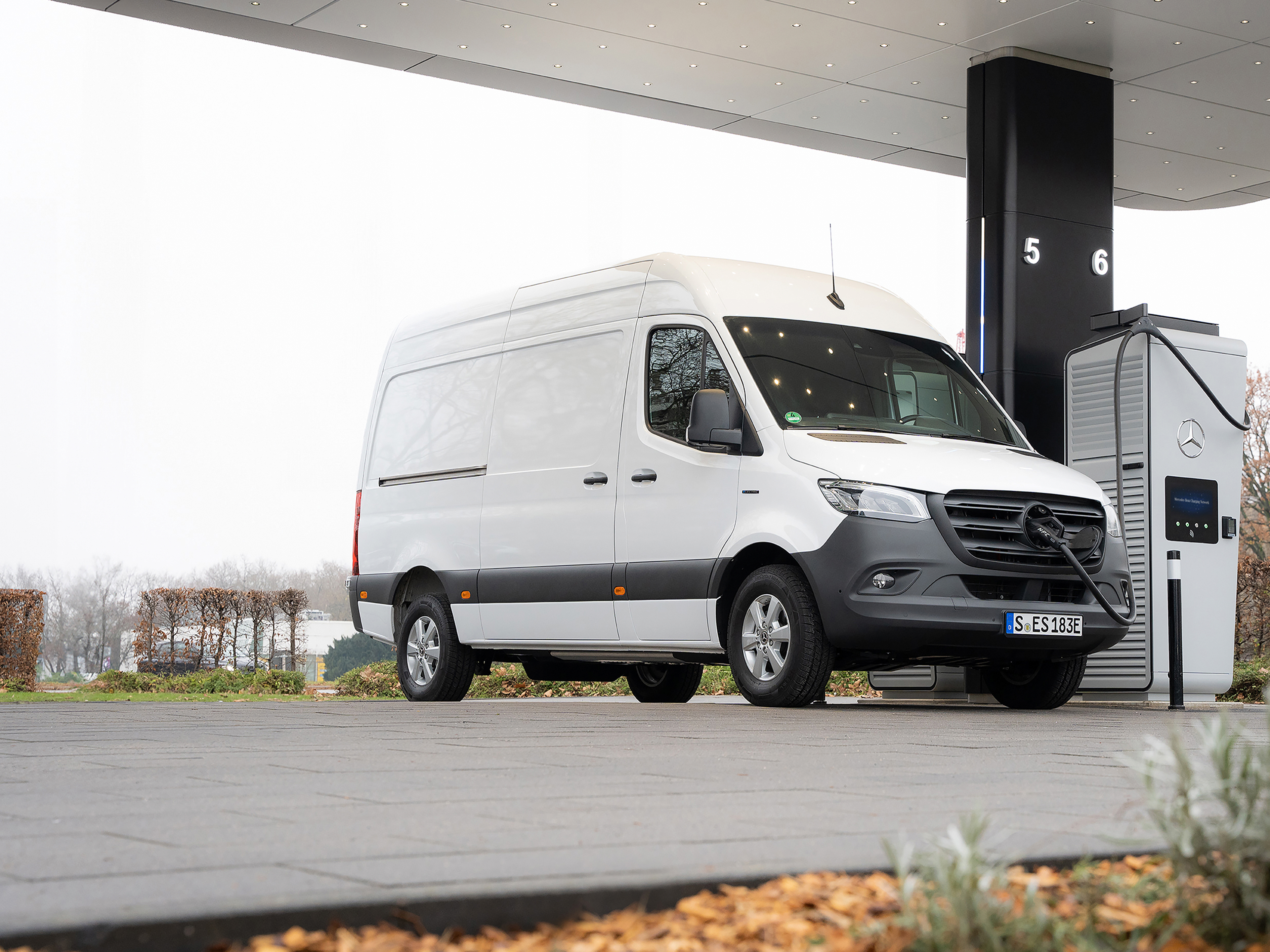 Ladelösungen | Mercedes-Benz Transporter. Eine weißer eSprinter Kastenwagen steht an einer Ladesäule be trübem Wetter.