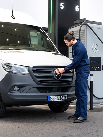 Eine Person vor einem weißen Mercedes-Benz Sprinter öffnet die Lade-Steckdose des Fahrzeugs.