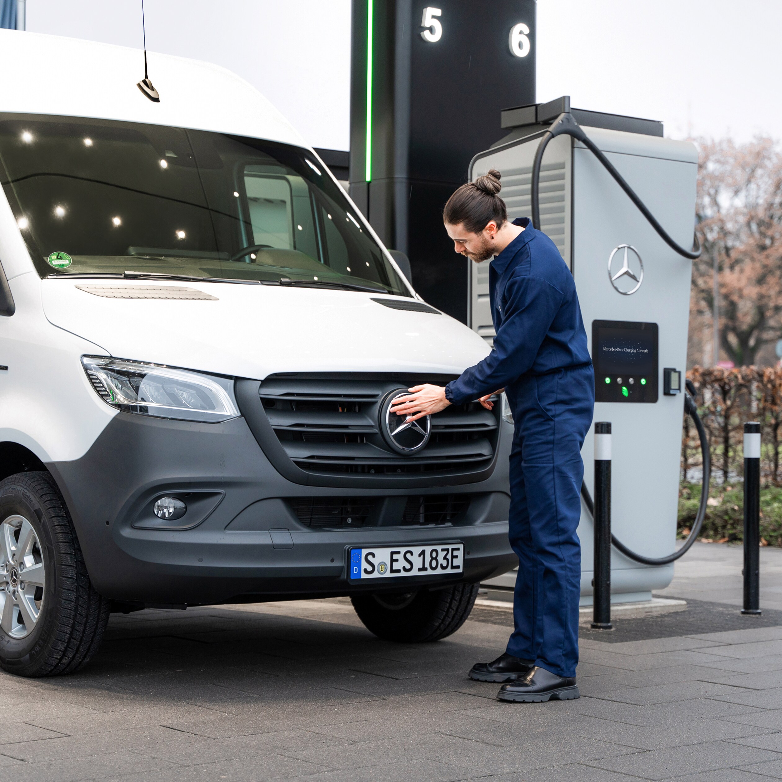 Ein Mann steht vor einem weißen Mercedes-Benz Transporter welcher vor einer Ladestation parkt.