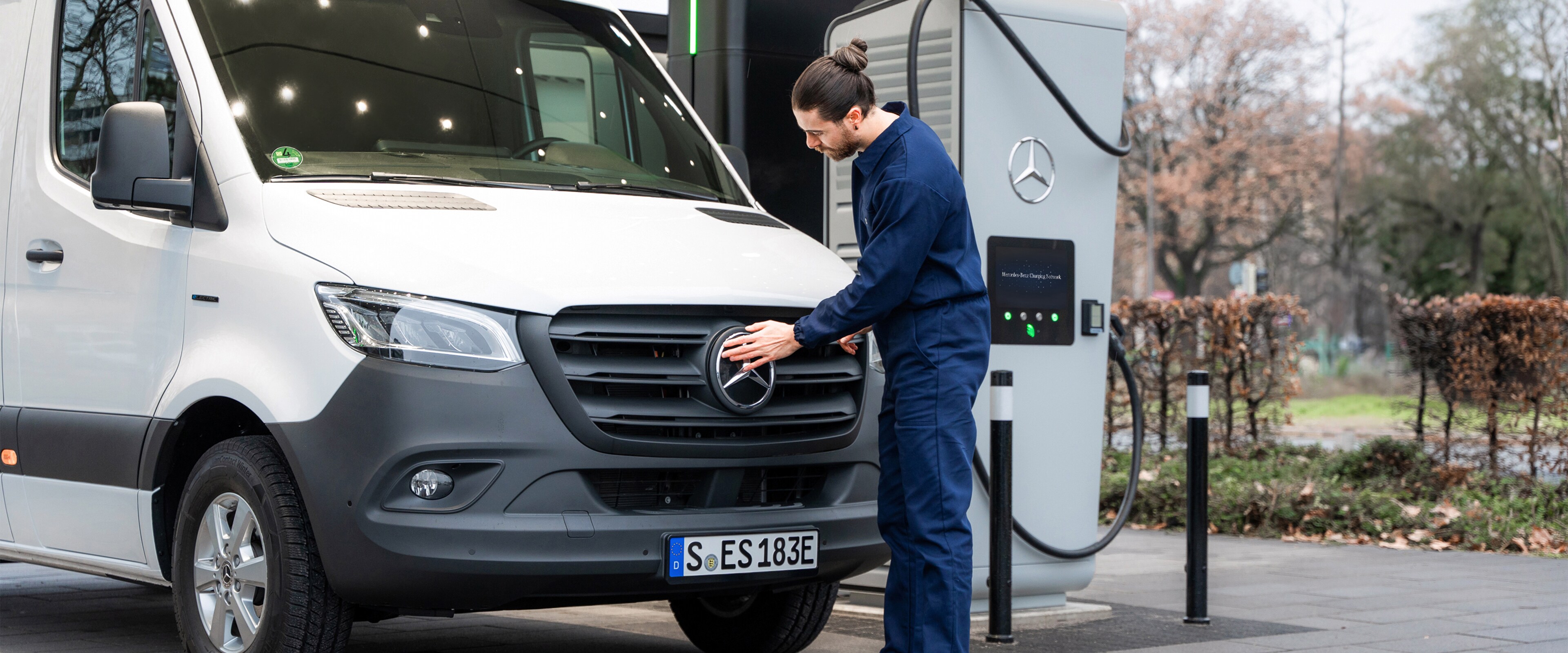 Ein Mercedes-Benz Transporter steht an einer Ladesäule und wird von einem Mann angeschlossen.
