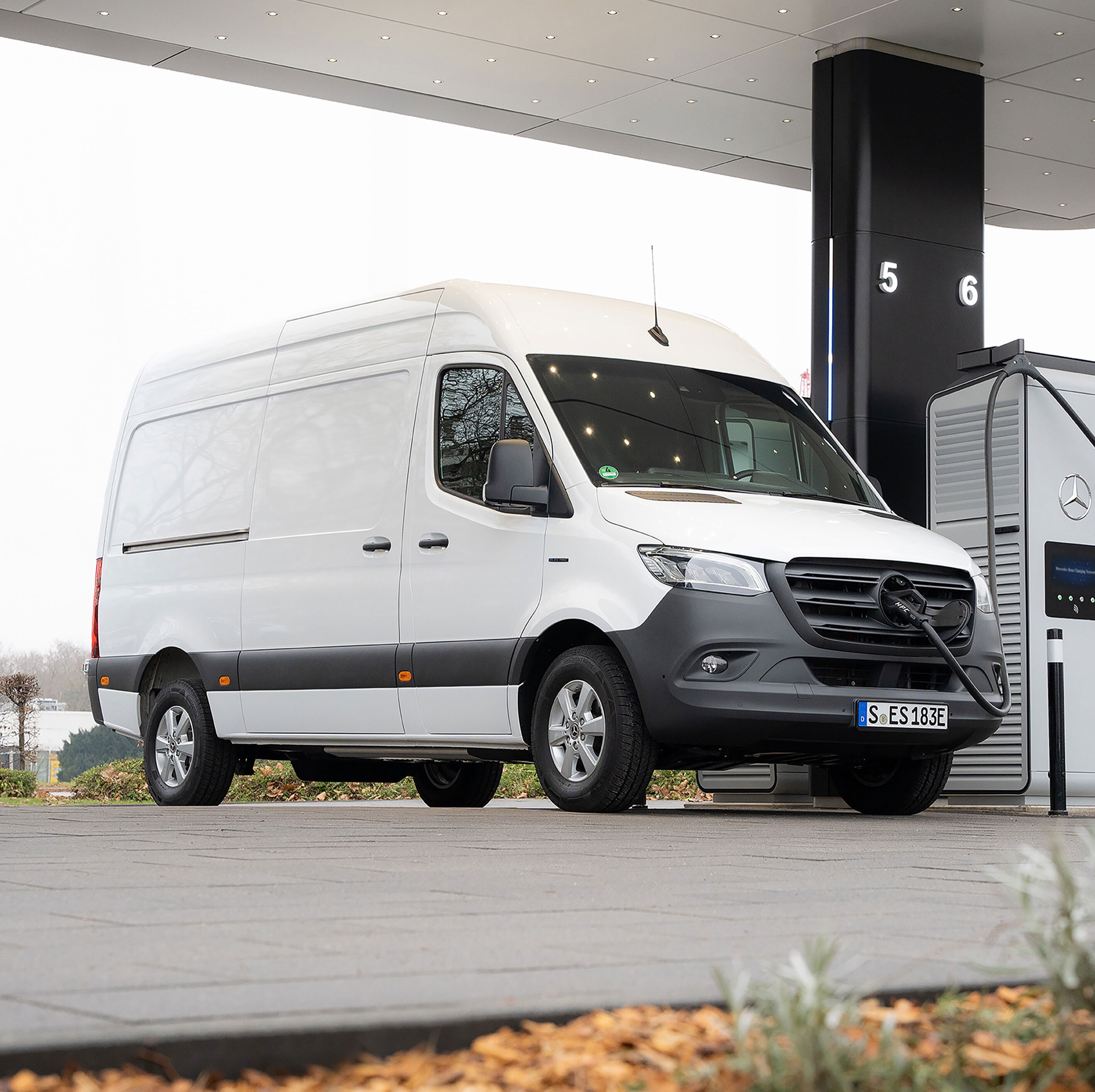 Ein weißer Sprinter Kastenwagen, wird an einer E-Ladesäule auf einem Parkplatz geladen.