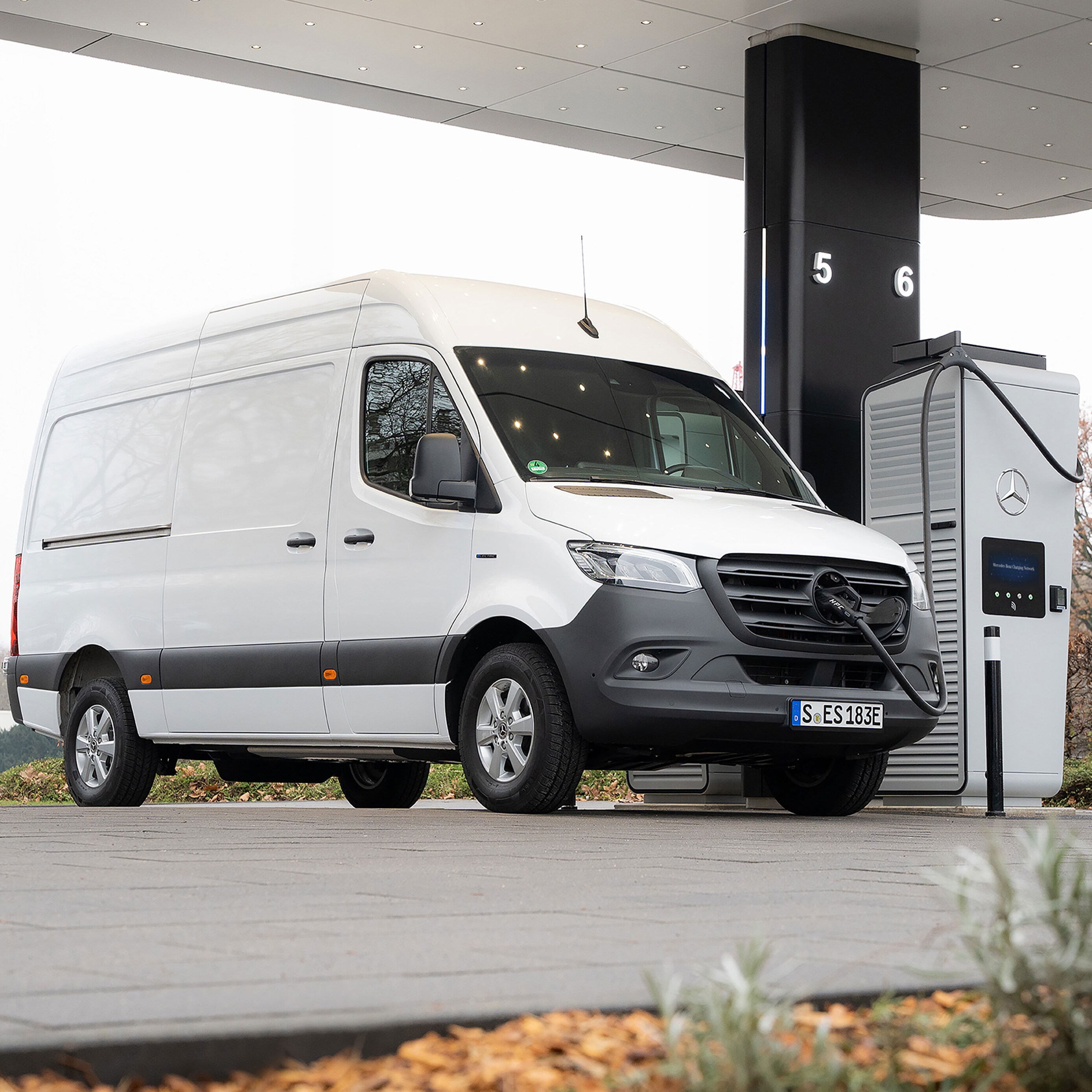Ein weißer Sprinter Kastenwagen, wird an einer E-Ladesäule auf einem Parkplatz geladen.